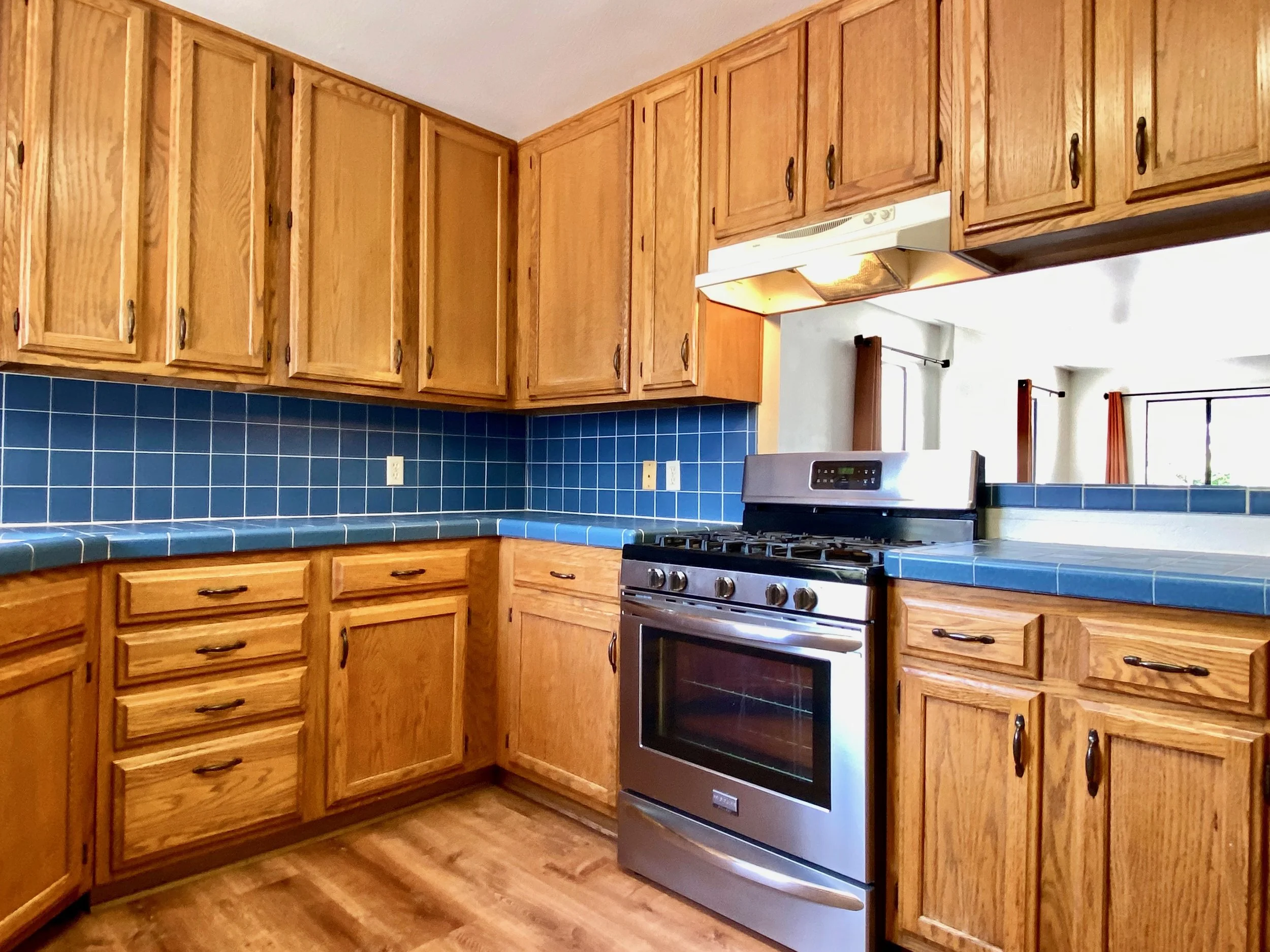 Kitchen with wooden cabinets, blue tiled countertop, and a stainless steel stove.
