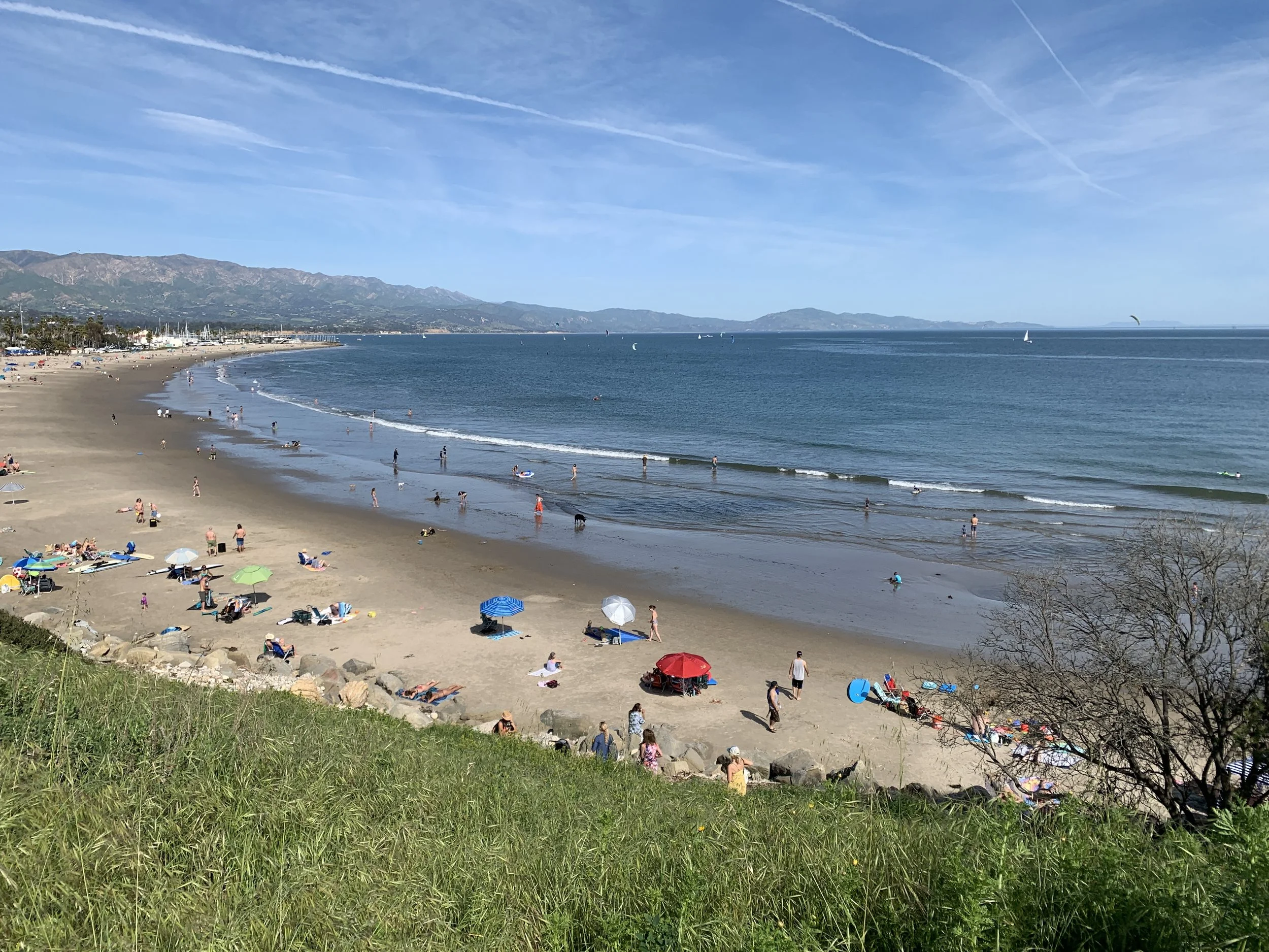 Photo of Leadbetter Beach, people playing in the water, and lounging under umbrellas on the beach.