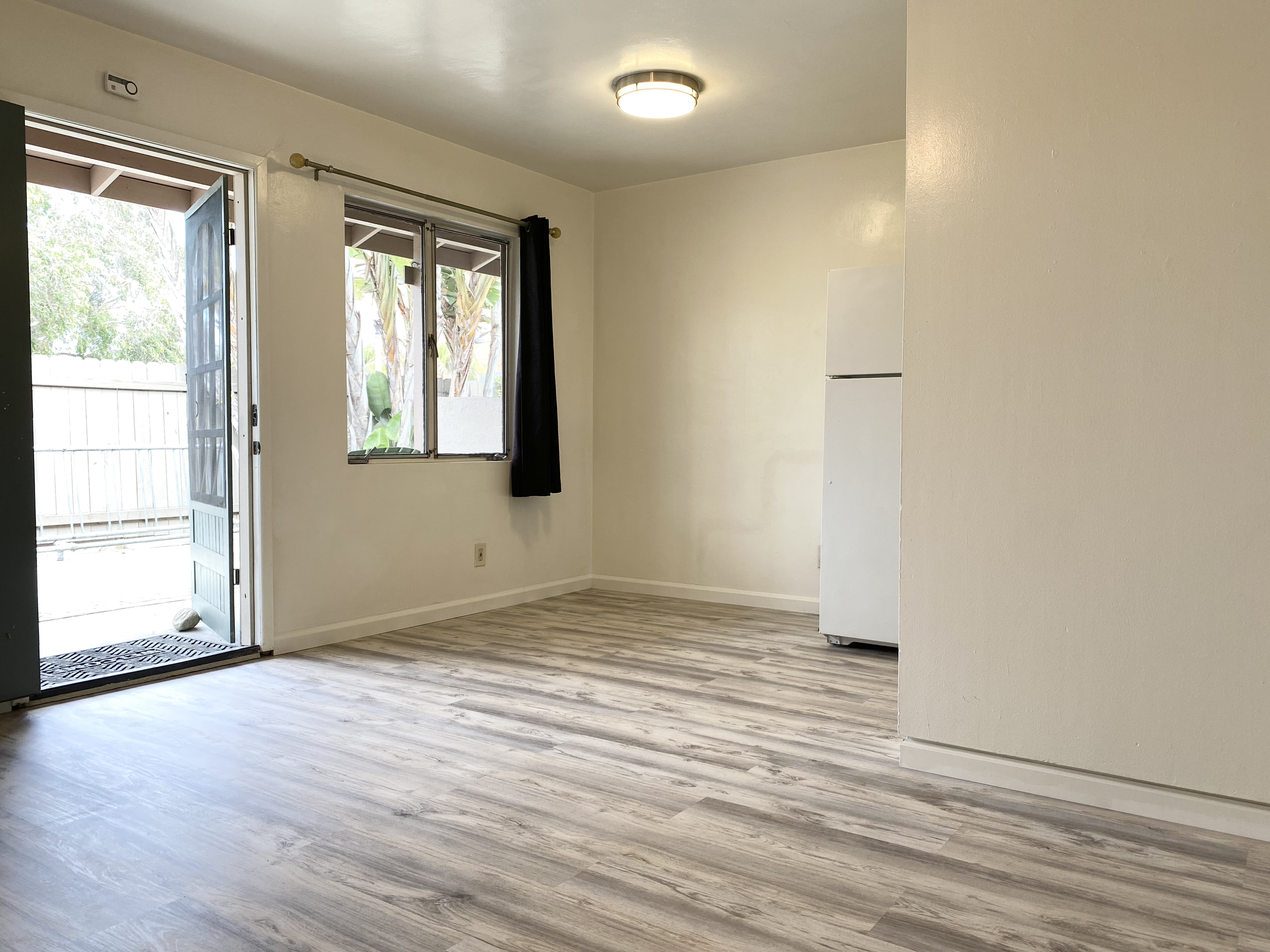 Empty room with open door, window, and vinyl wood-like flooring.