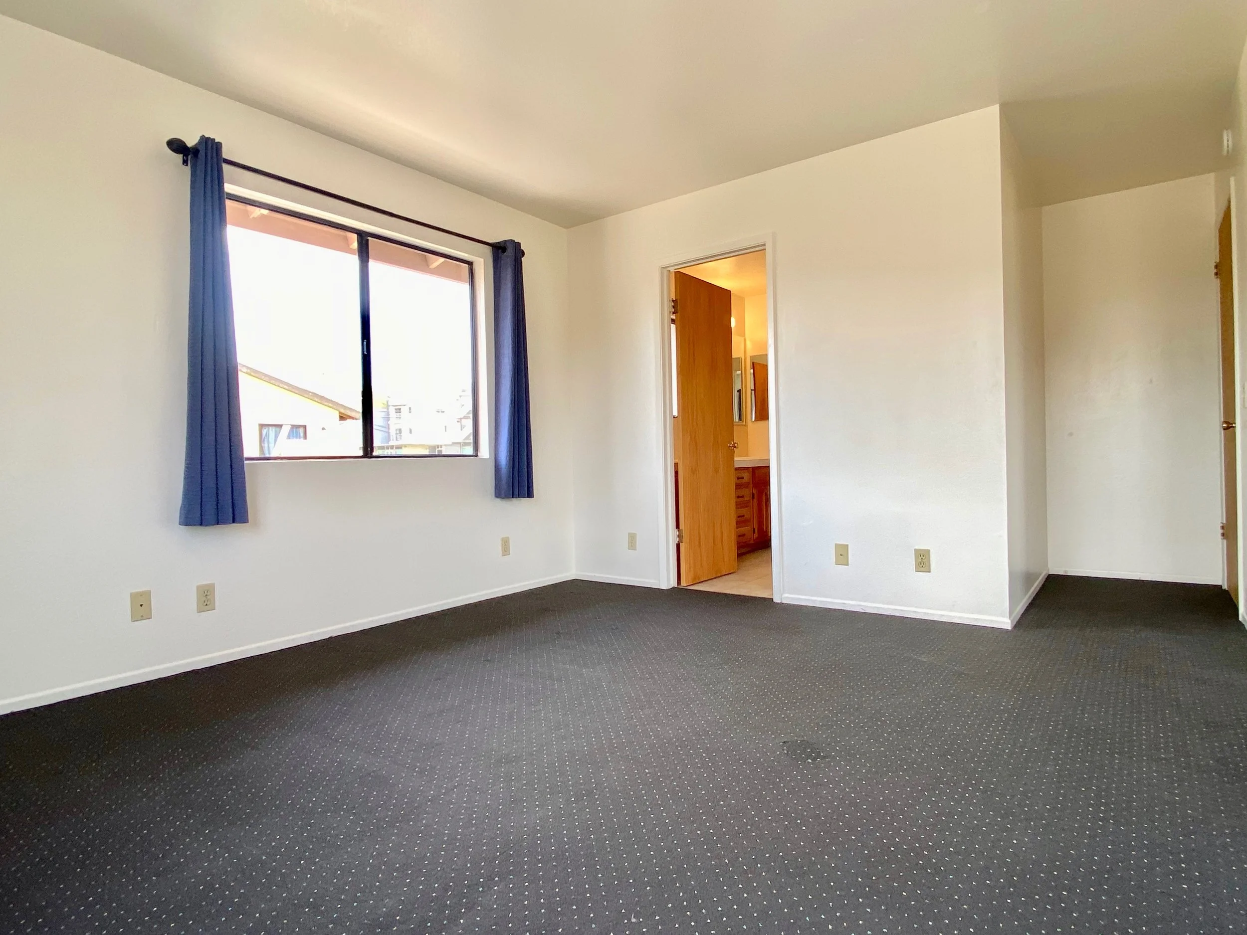 Empty room with a window and an open door leading to a bathroom.