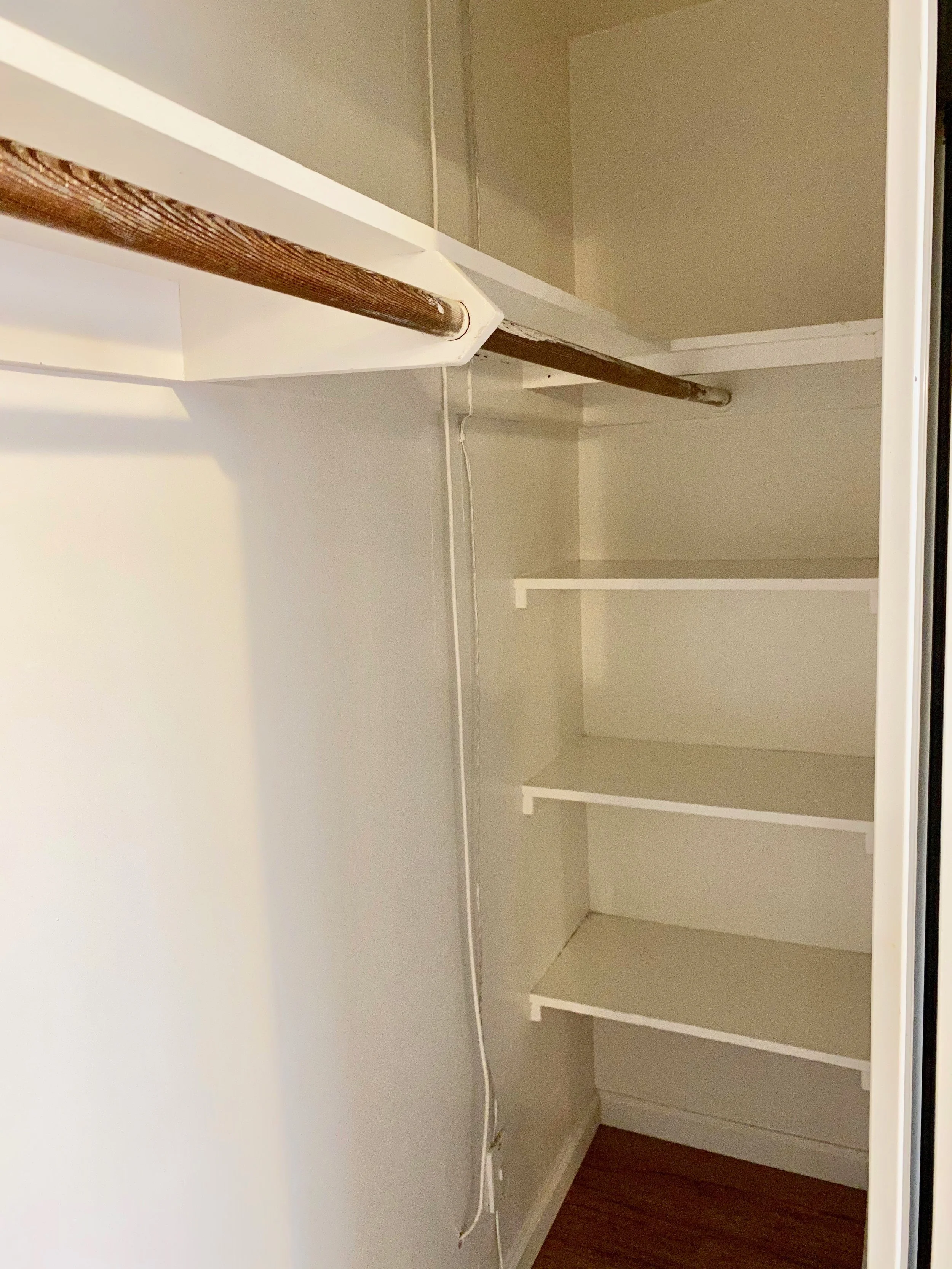 Empty closet with white shelves, white walls, wooden floor.