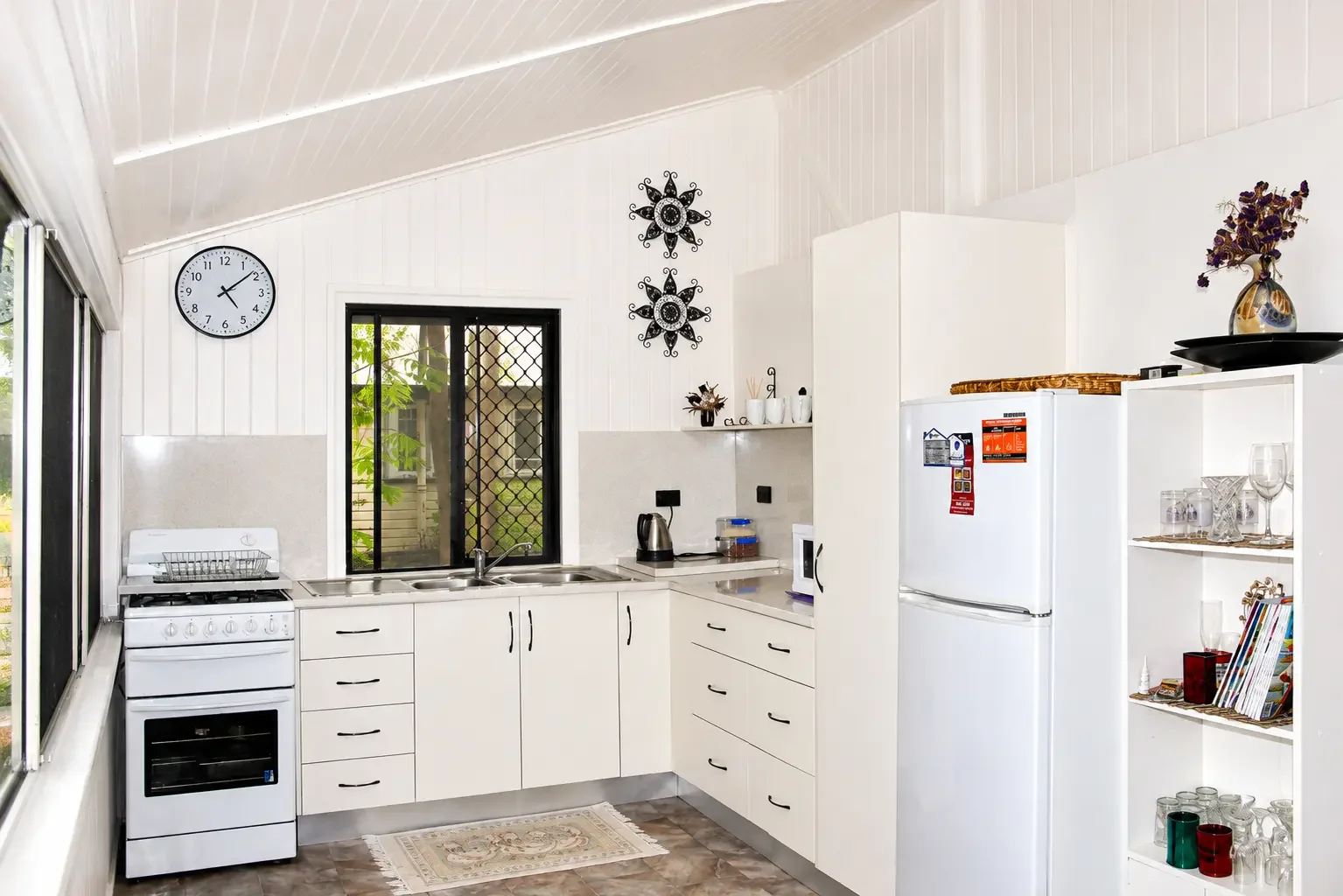 White kitchen cabinetry with open shelving, integrated appliances and a window above the sink.
