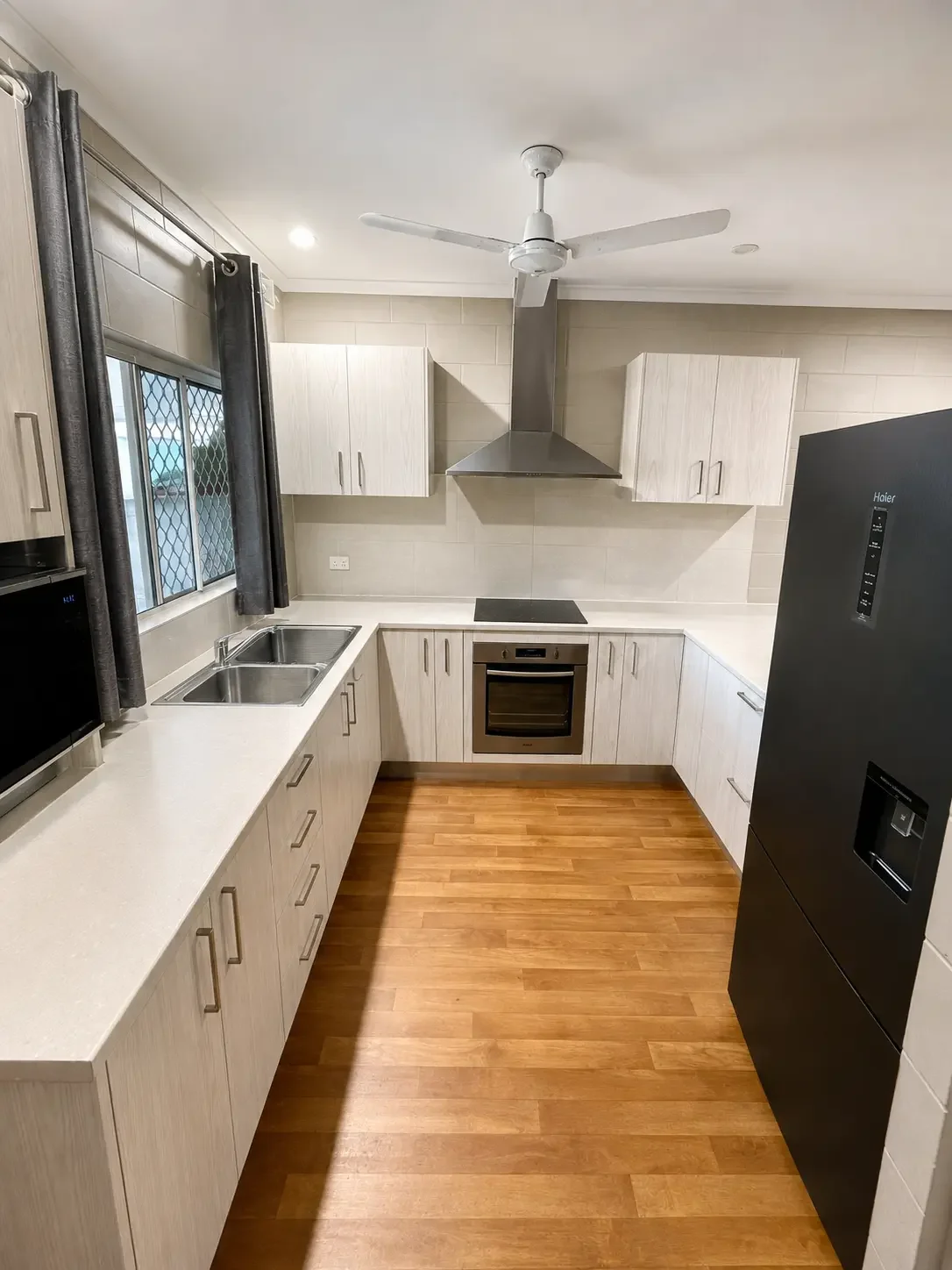 White kitchen cabinetry with black appliances, tiled splashback and timber flooring.
