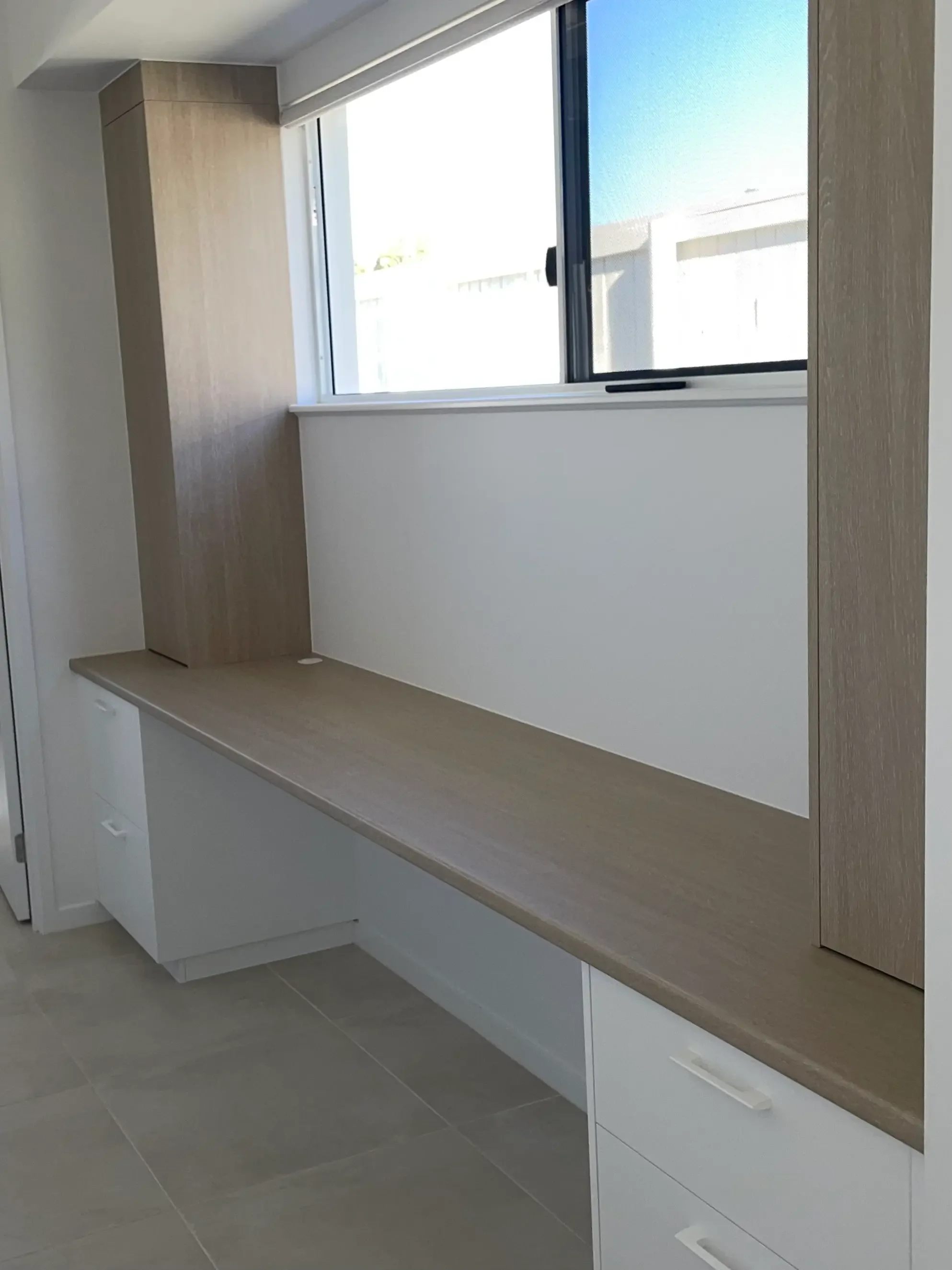 White and timber-look built-in cabinetry fitted beneath a window.

