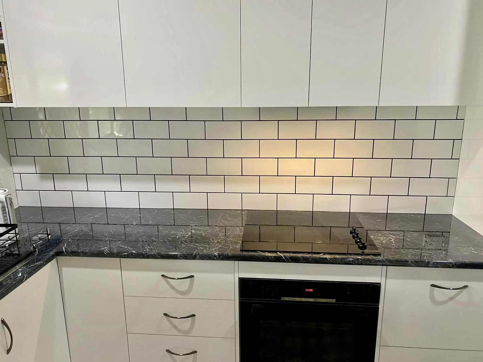 White kitchen cabinetry with dark benchtops, built-in oven and white subway tile splashback.

