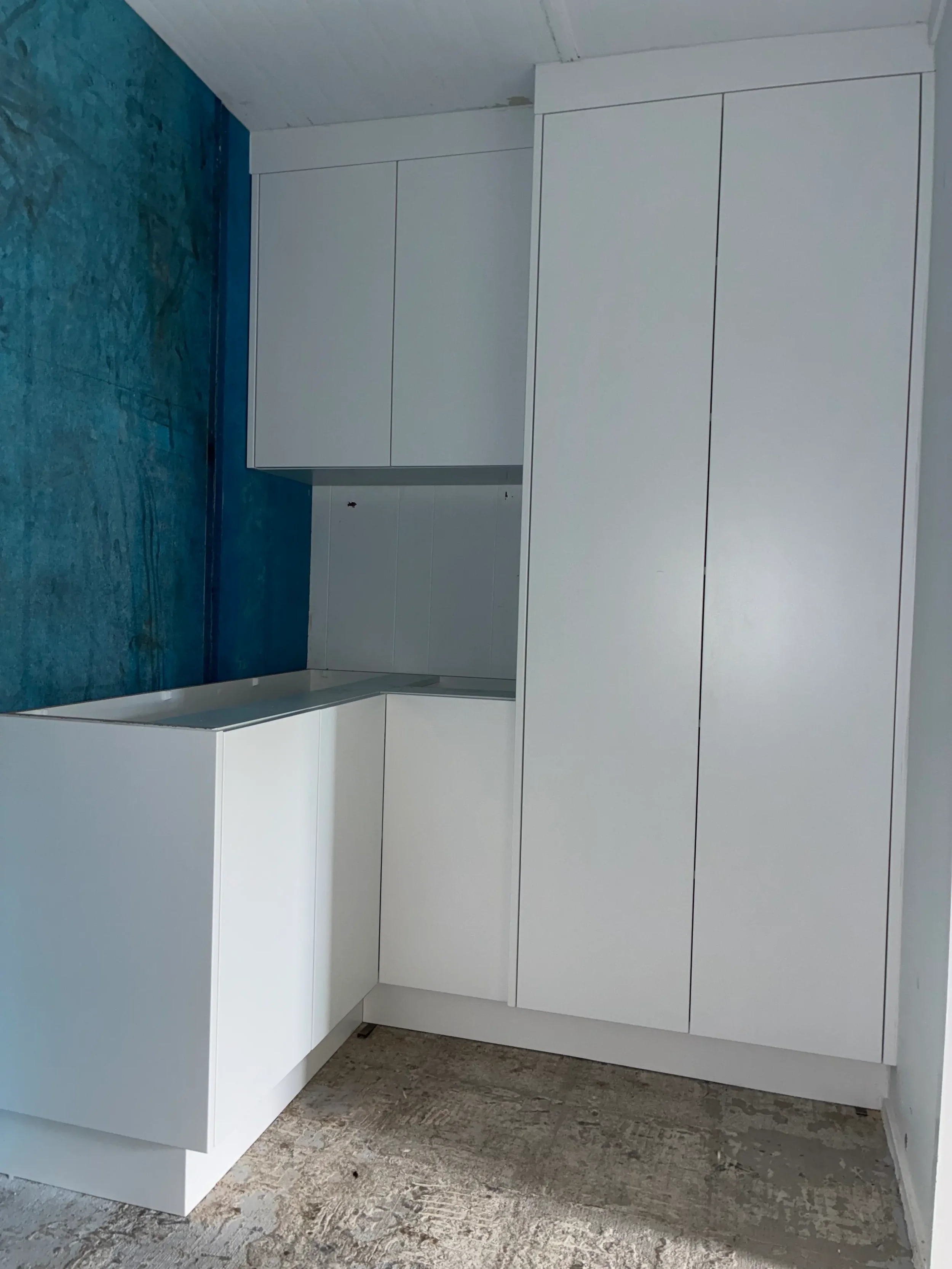 White floor-to-ceiling cabinetry with integrated open shelving and blue feature wall.
