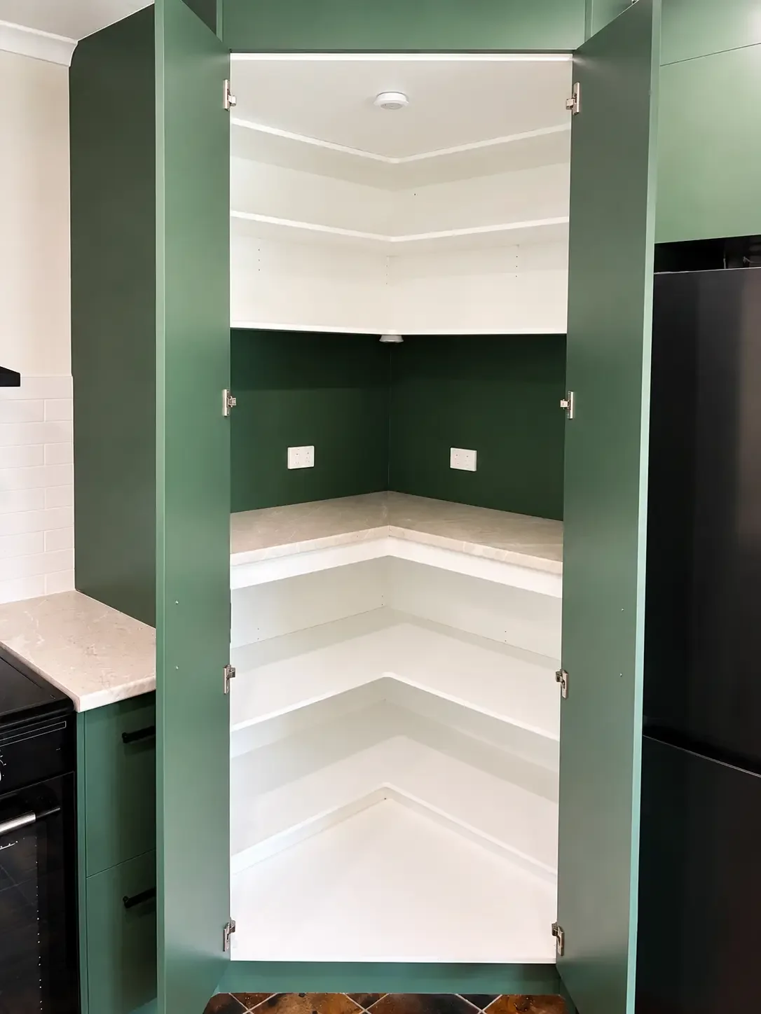 Open tall green pantry cabinet with adjustable internal shelving and power outlets.
