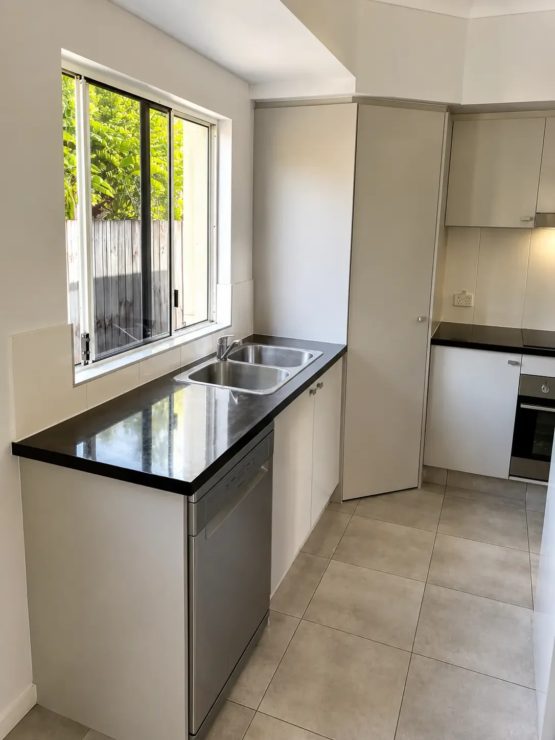 White kitchen cabinetry with dark benchtops and a double sink beneath the window.
