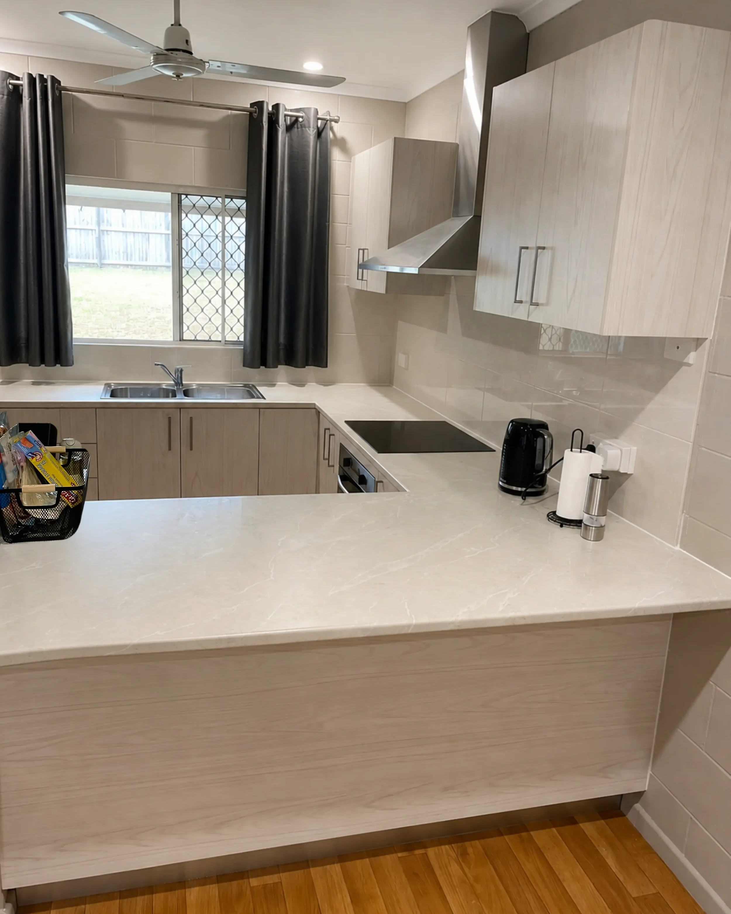 Light-coloured kitchen cabinetry with a sink beneath the window and tiled splashback.

