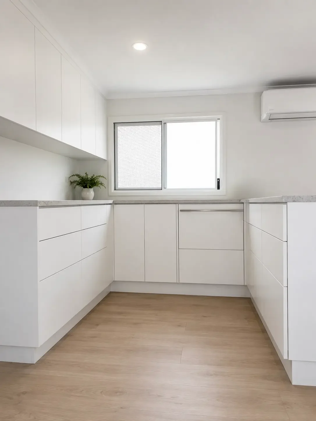 White kitchen cabinetry with grey benchtops and timber-look flooring.
