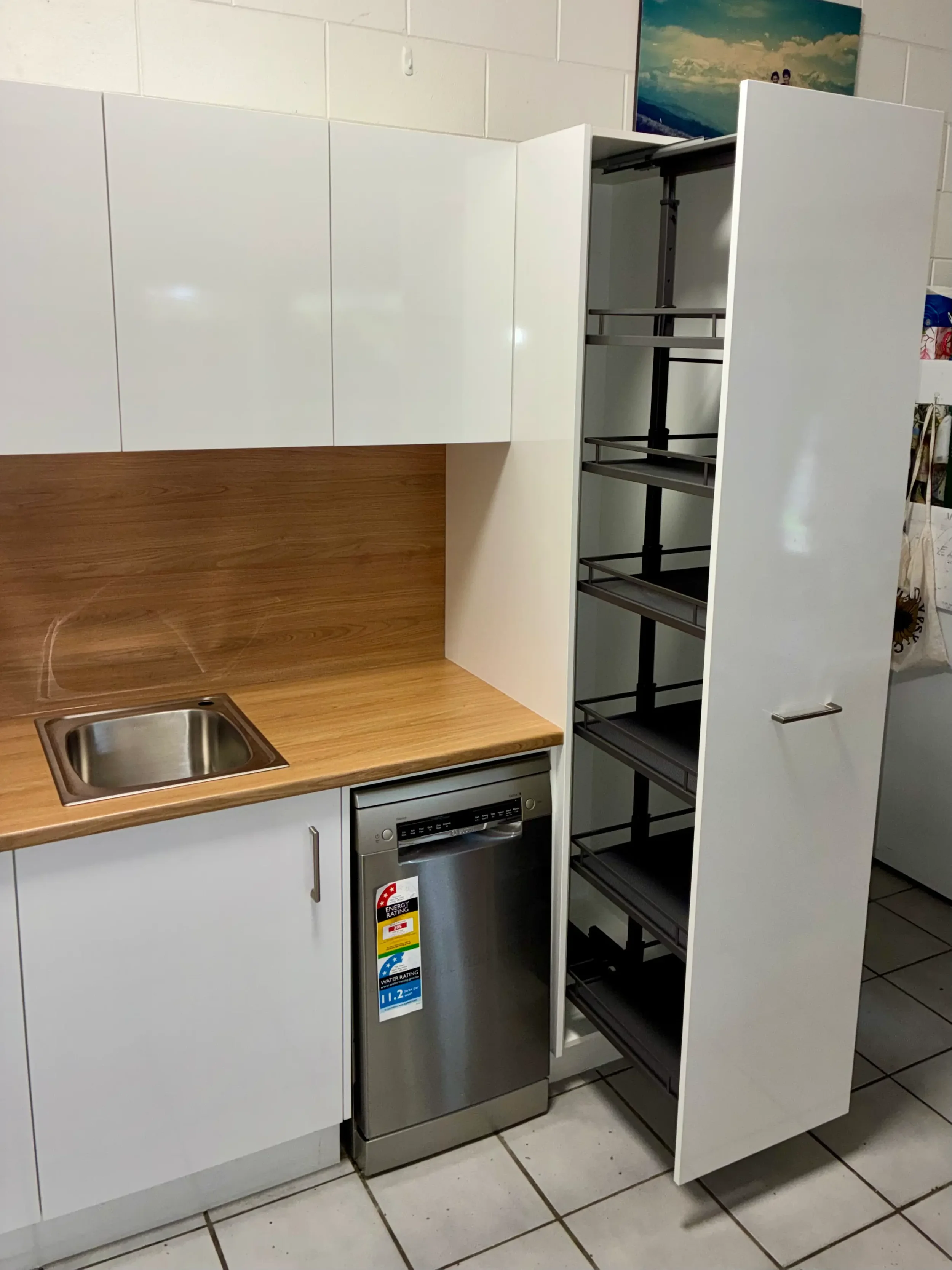 White kitchen cabinetry with timber benchtop, stainless steel sink and open wire shelving.
