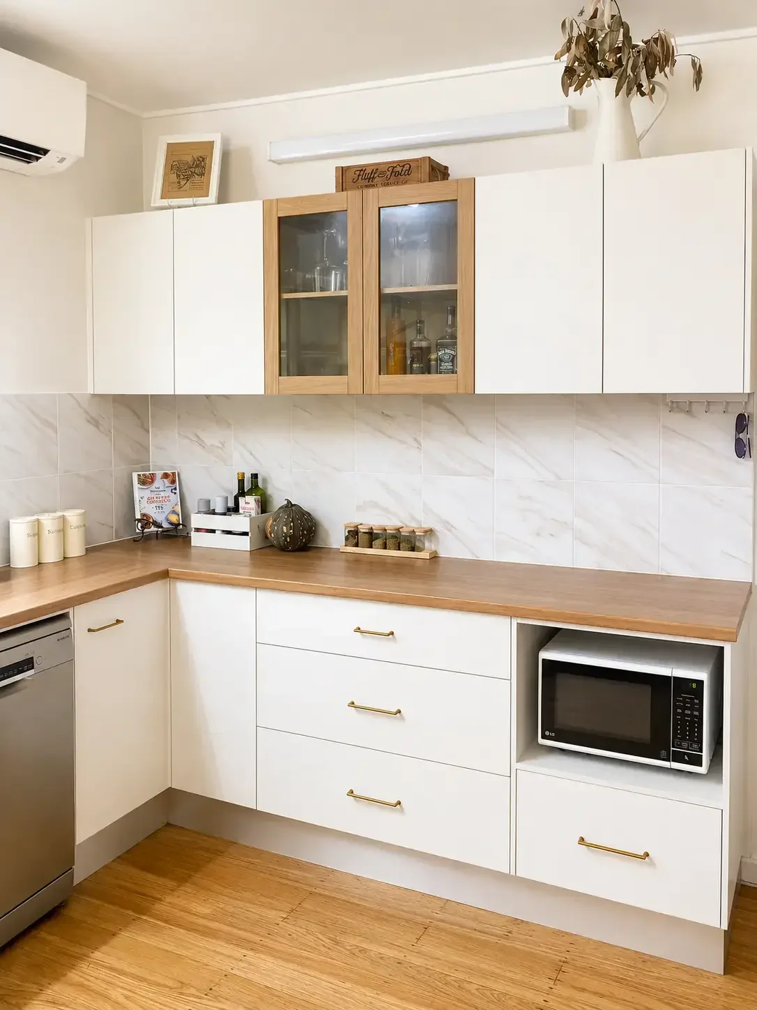 White kitchen cabinetry with timber benchtops, built-in microwave and overhead storage.

