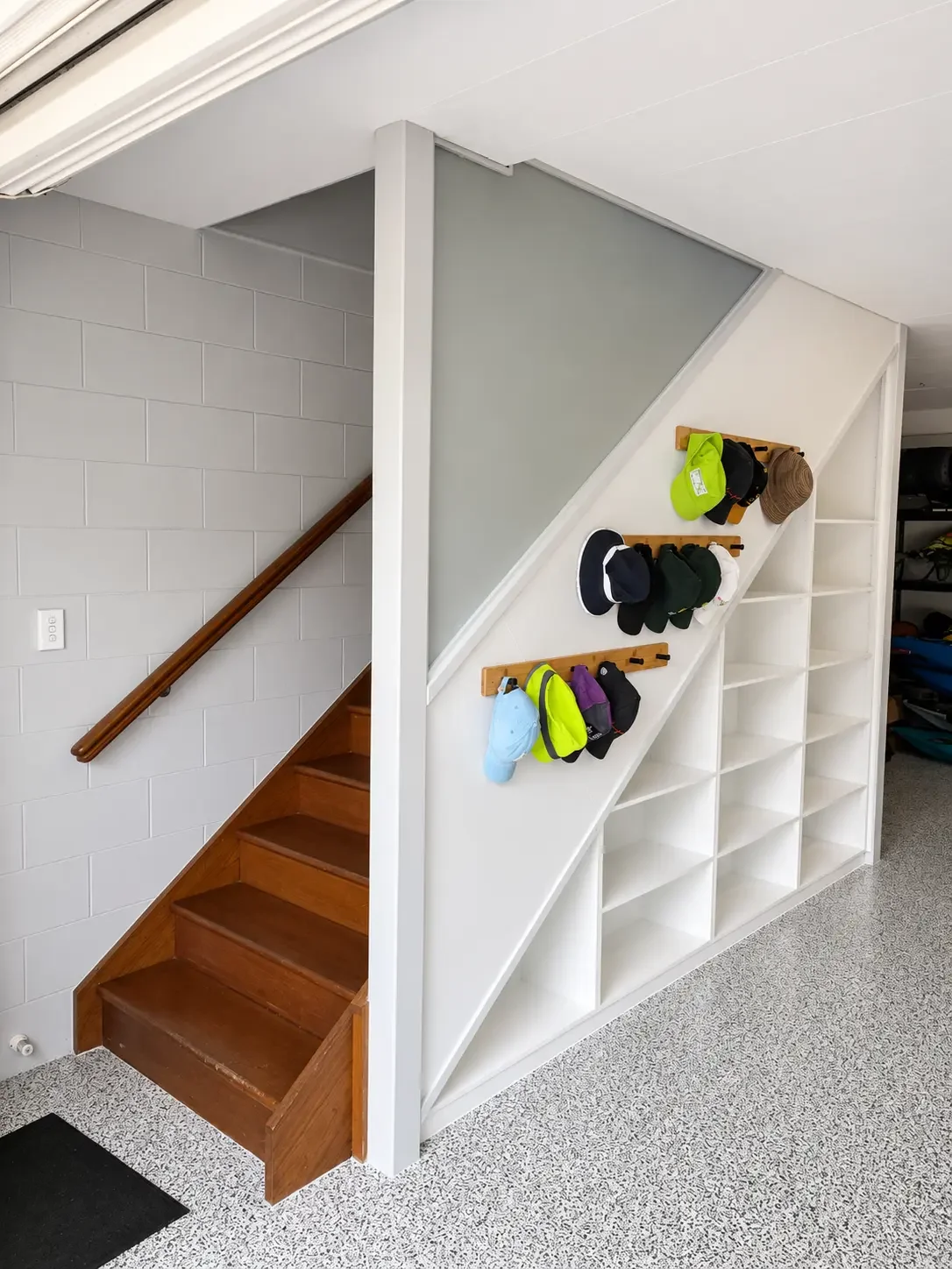White under-stair cabinetry with open shelving and wall hooks beside the staircase.
