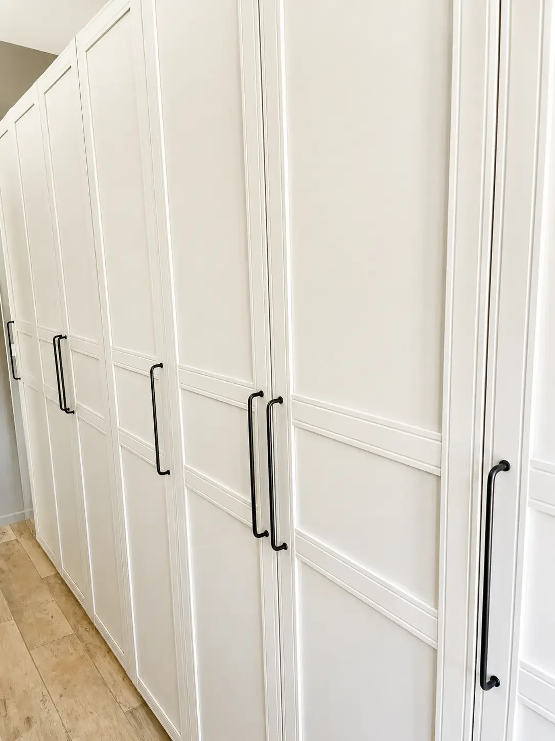 White built-in wardrobe cabinetry with black handles and matching wall hooks.
