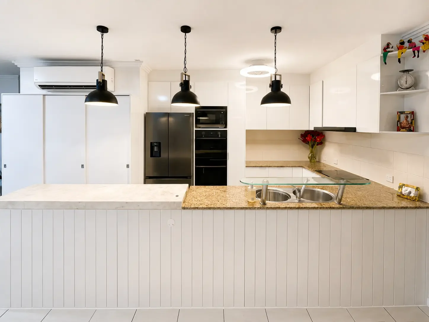 White custom kitchen cabinetry with stone benchtops, black pendant lights and breakfast bar.
