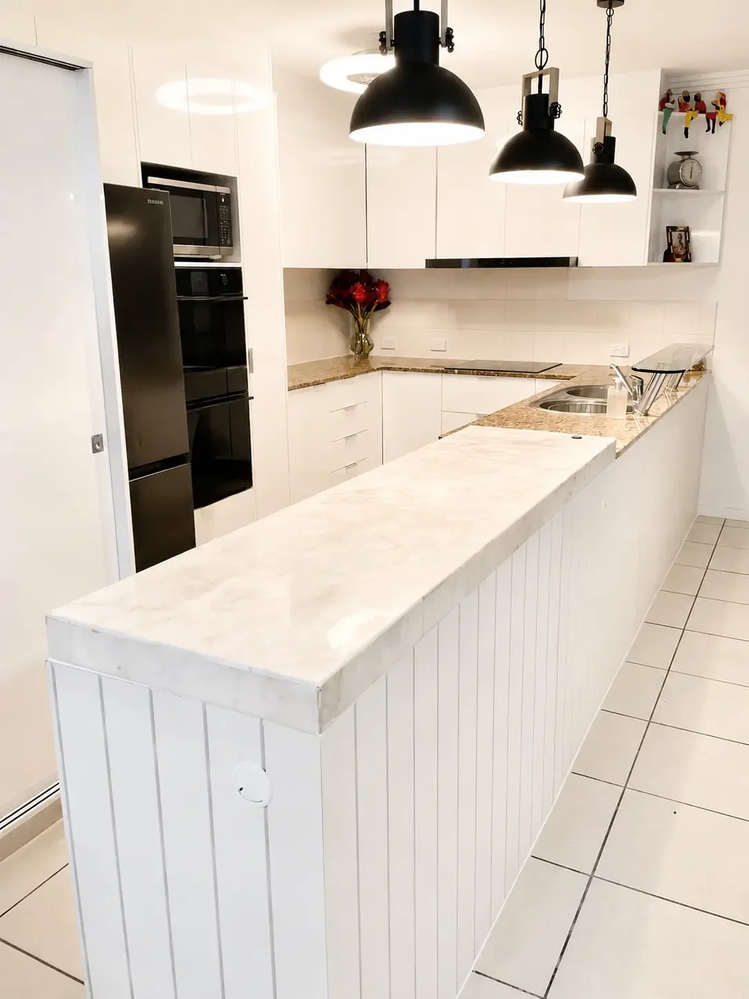 White kitchen island cabinetry with stone benchtop and integrated sink.
