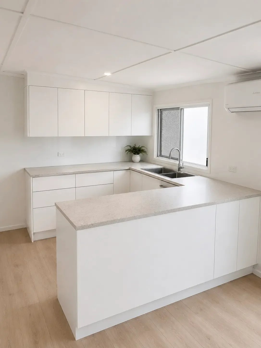 White custom kitchen cabinetry with an island bench, stone benchtops and a window above the sink.
