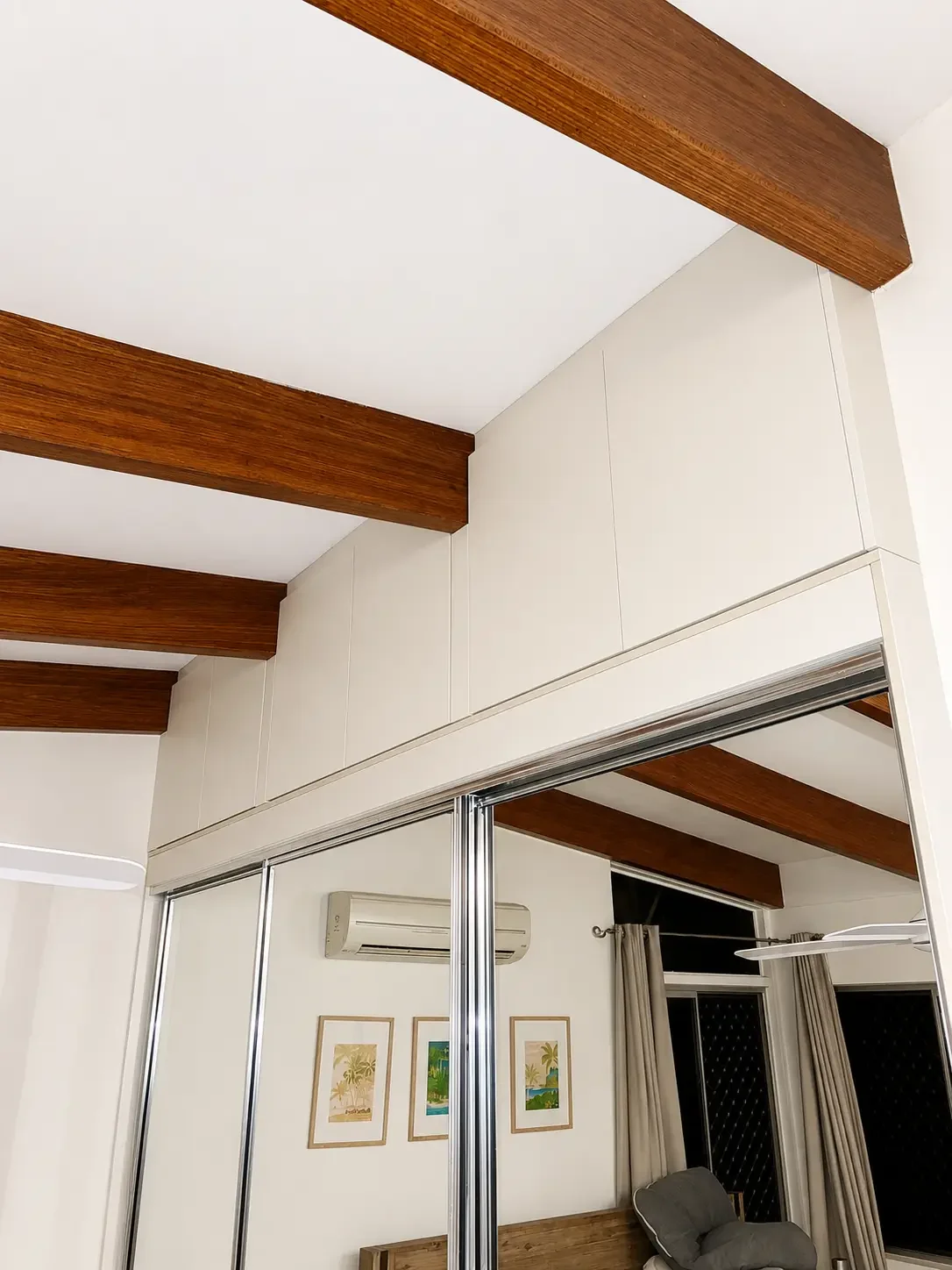Mirrored sliding wardrobe doors fitted within a bedroom with exposed timber ceiling beams.
