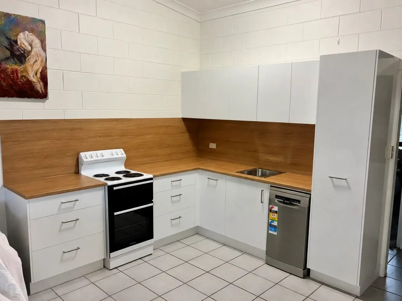 L-shaped white kitchen cabinetry with timber benchtops and integrated appliances.
