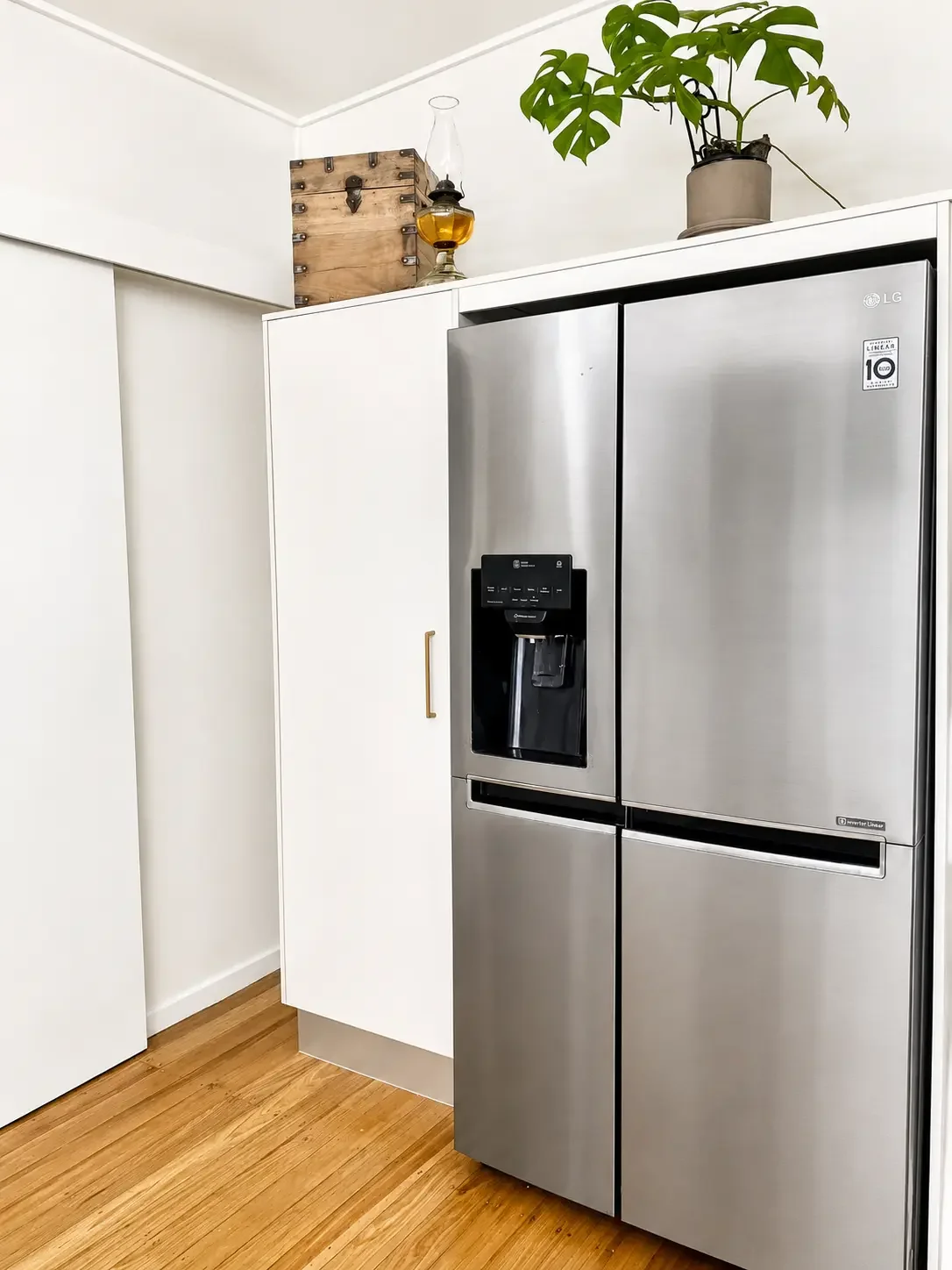 Stainless steel refrigerator beside white custom kitchen cabinetry with timber flooring.
