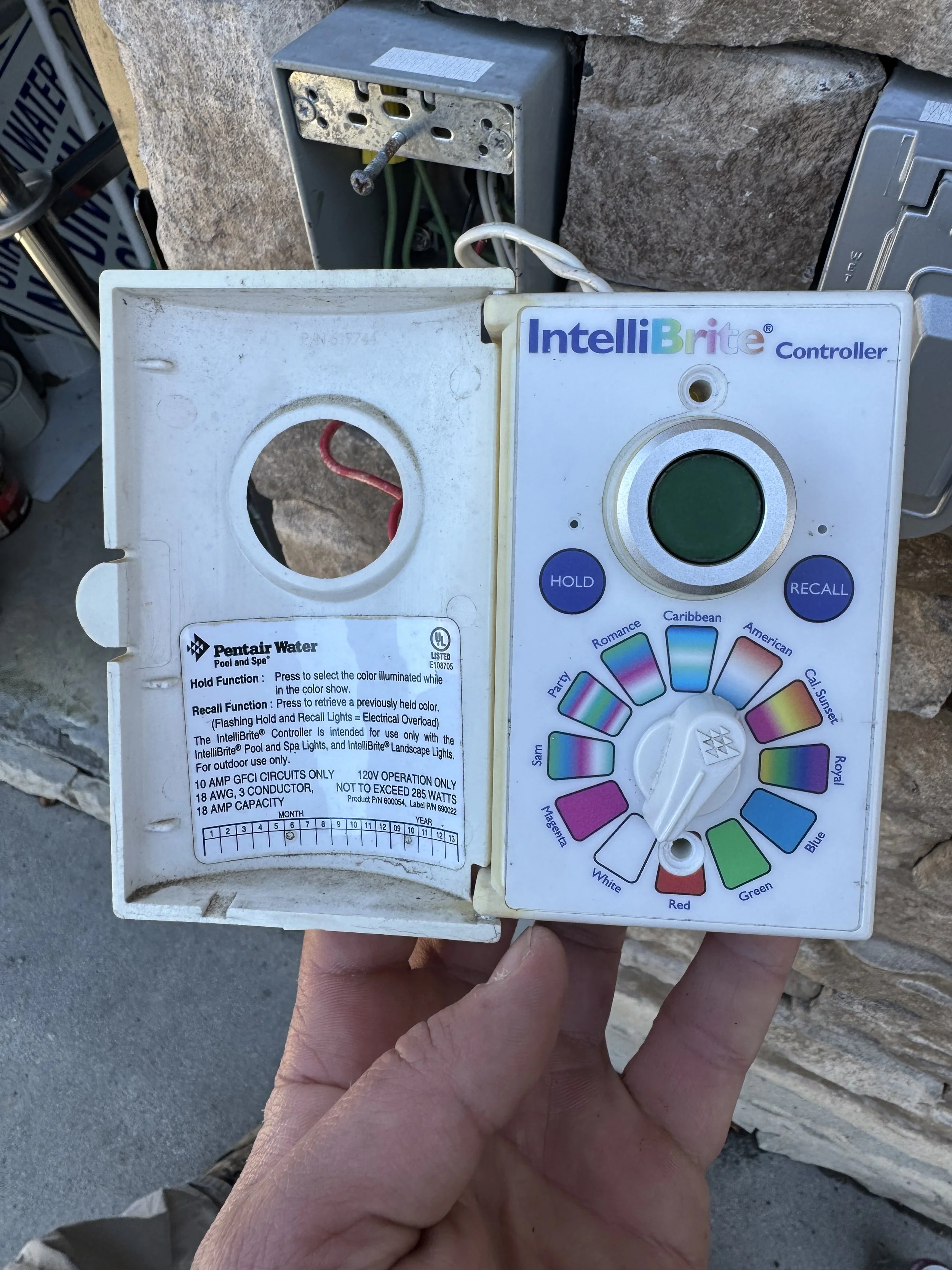 A hand holding a colorful control panel for a pool or spa lighting system, with a logo reading 'Pentair Water'.
