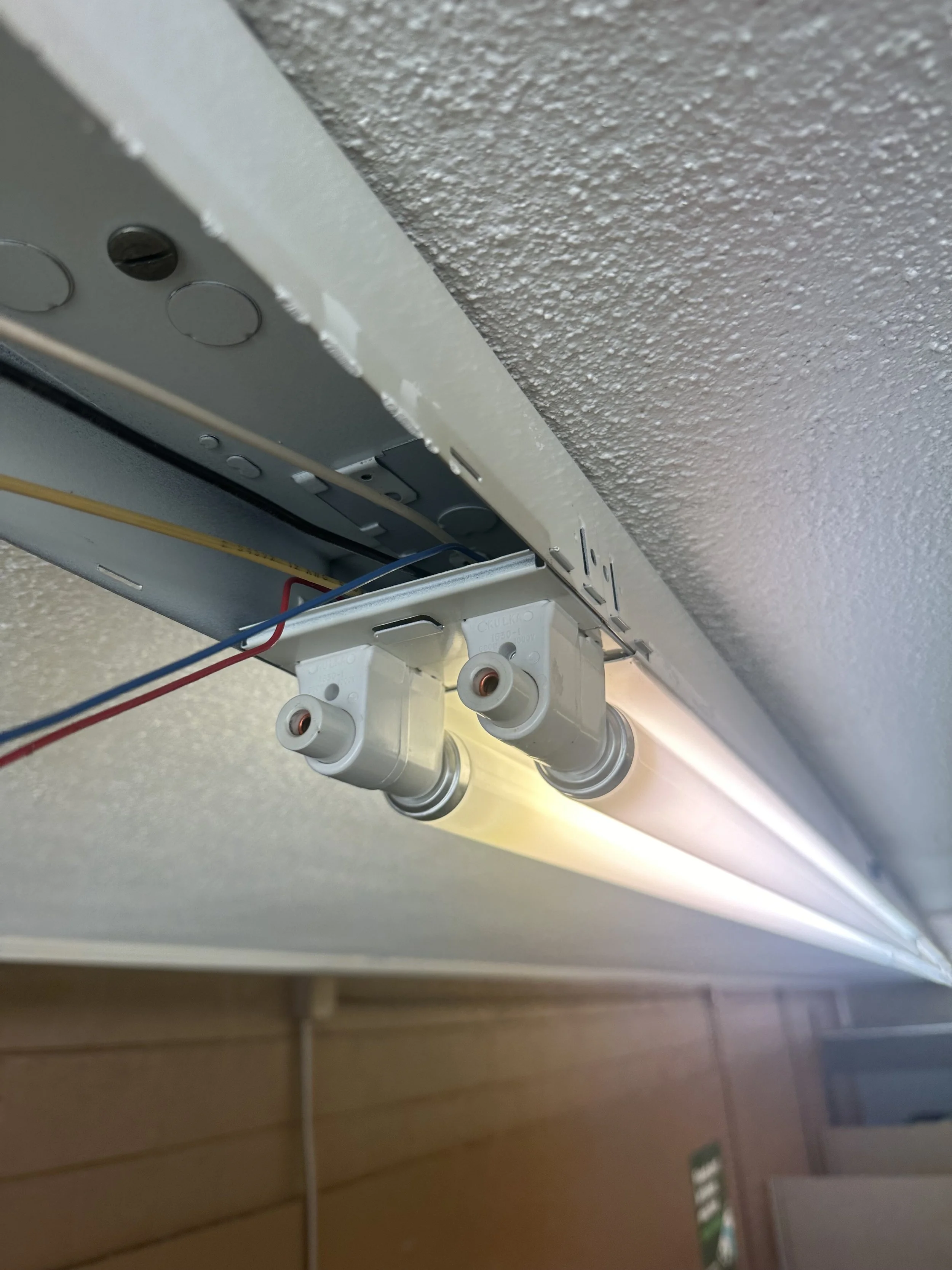 Close-up of electrical wiring and sockets mounted on a ceiling with a textured wall.