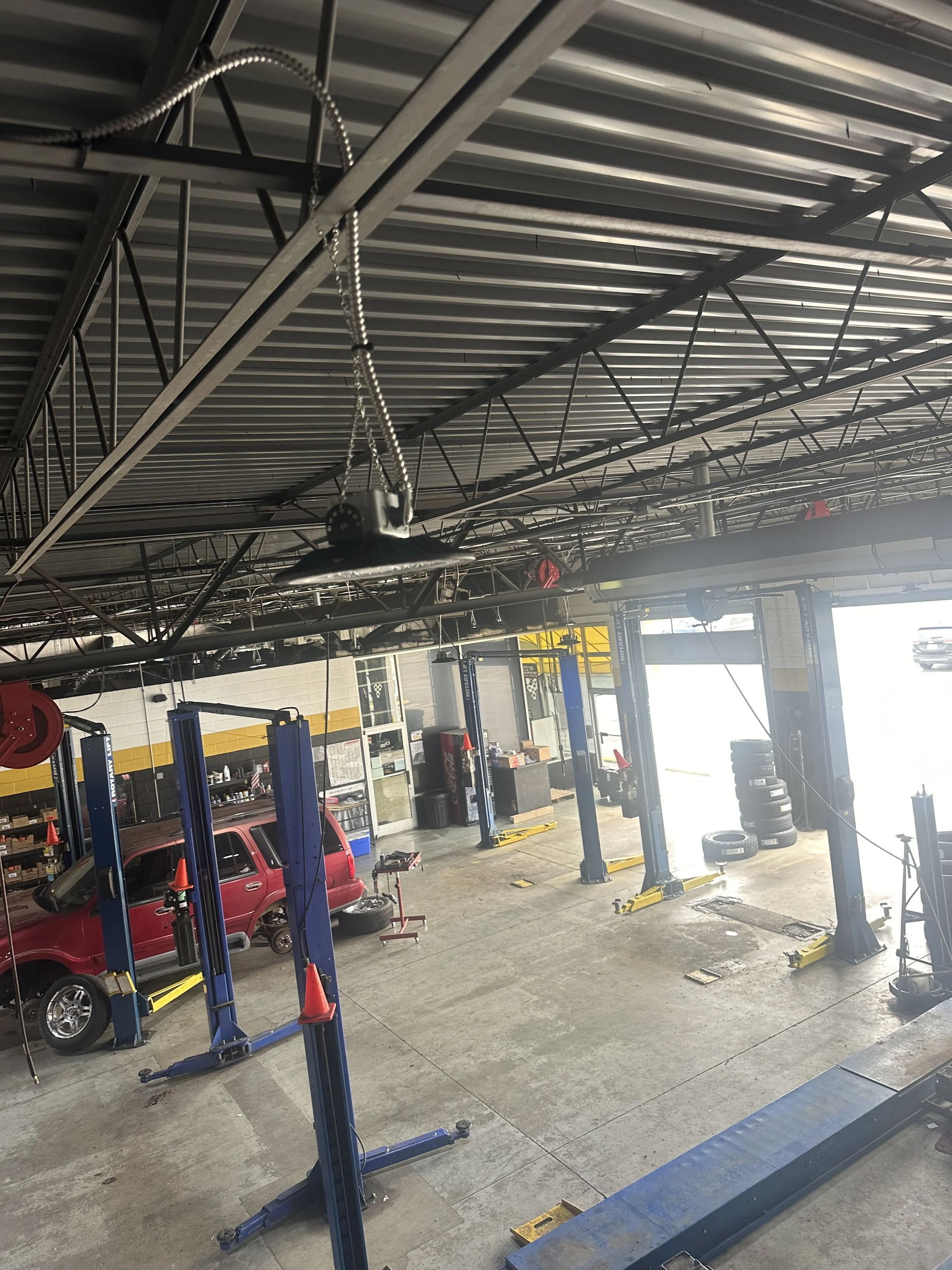 View inside an automotive repair shop with car lifts, a red minivan on one lift, and various tires and tools around.