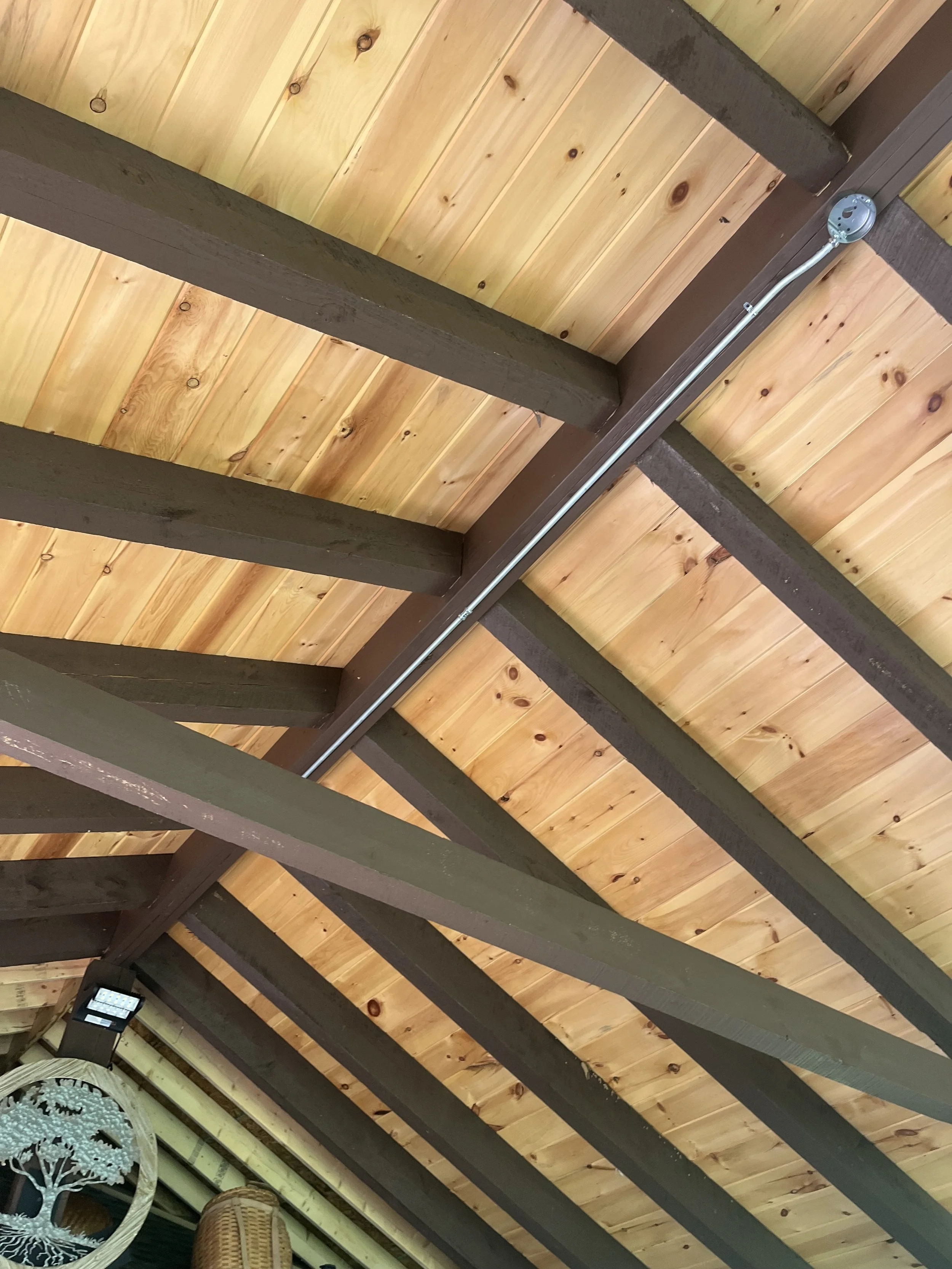 Ceiling view showing wooden planks and dark brown beams with a metal conduit running along the beams.
