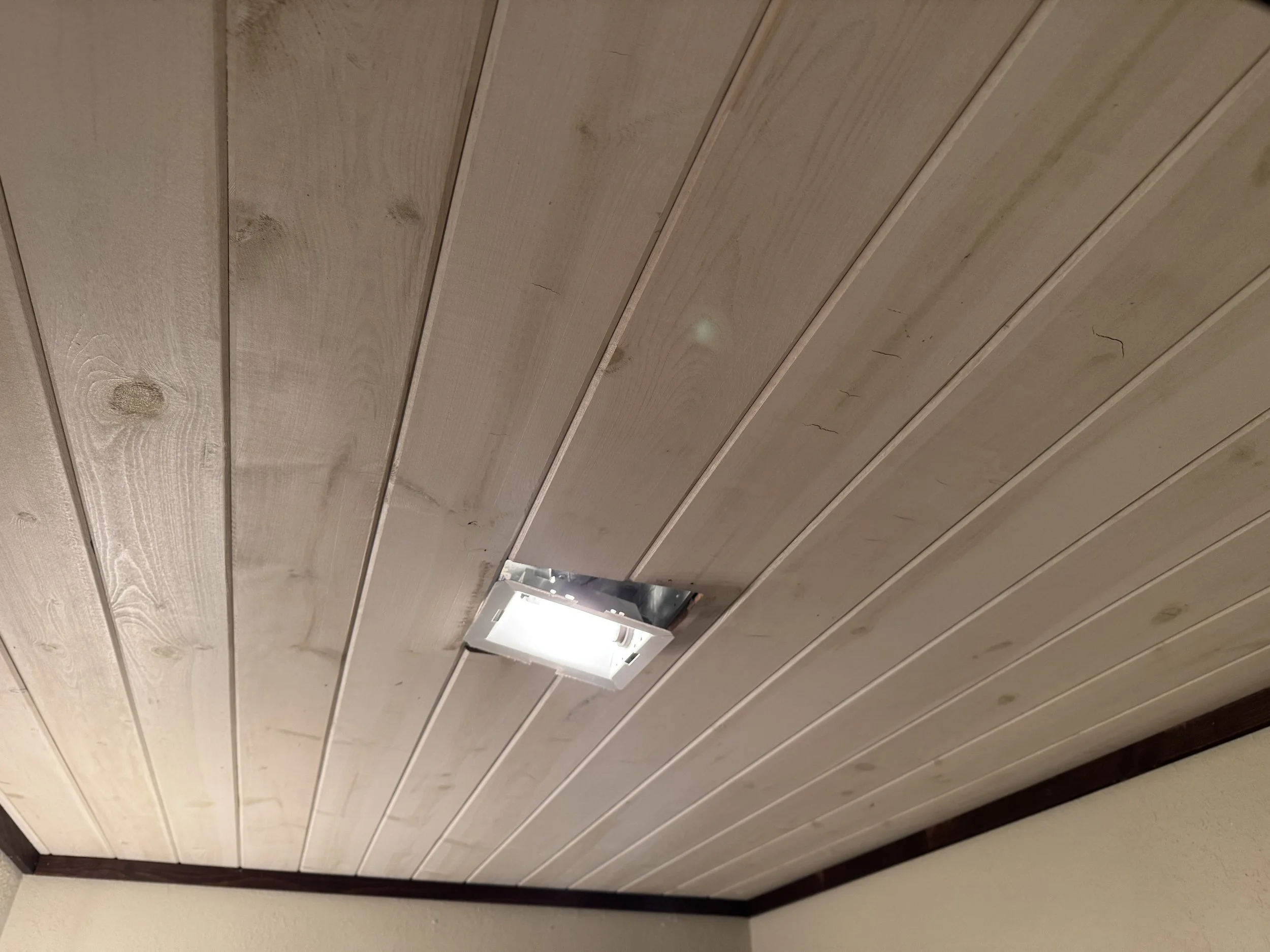 Wood-paneled ceiling with a vent and a visible light source at the bottom of the image.