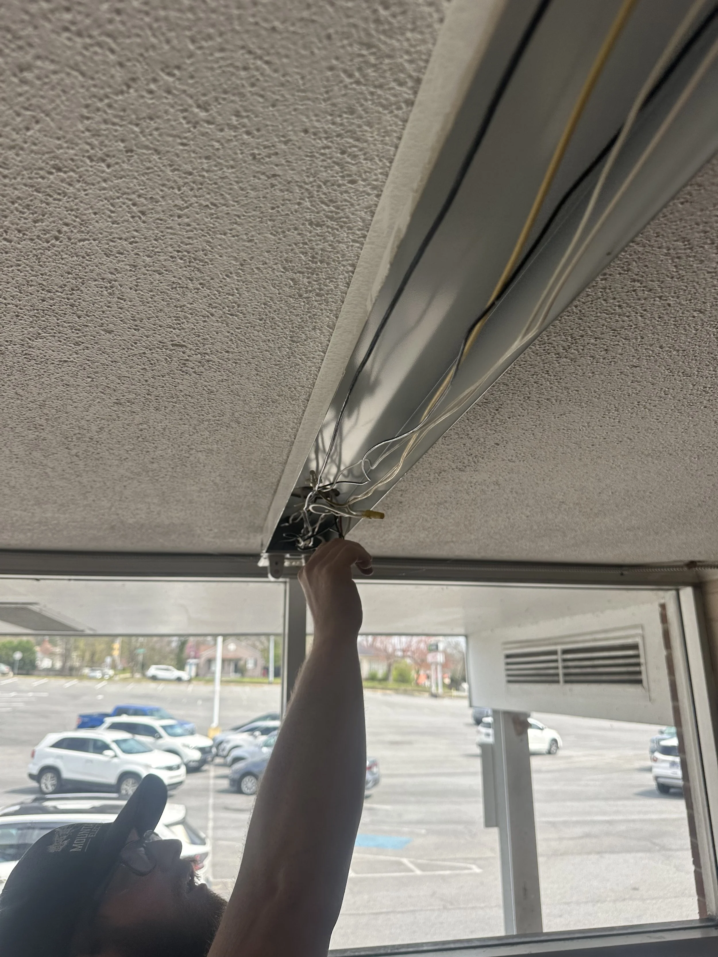 Person installing a ceiling ventilation system near a window in a parking lot.