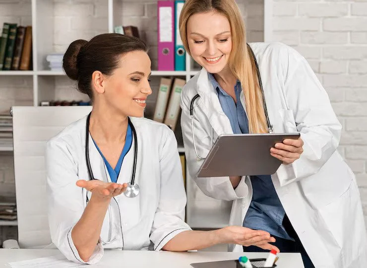 Two female doctors in white coats discussing and reviewing a clipboard in a medical office.