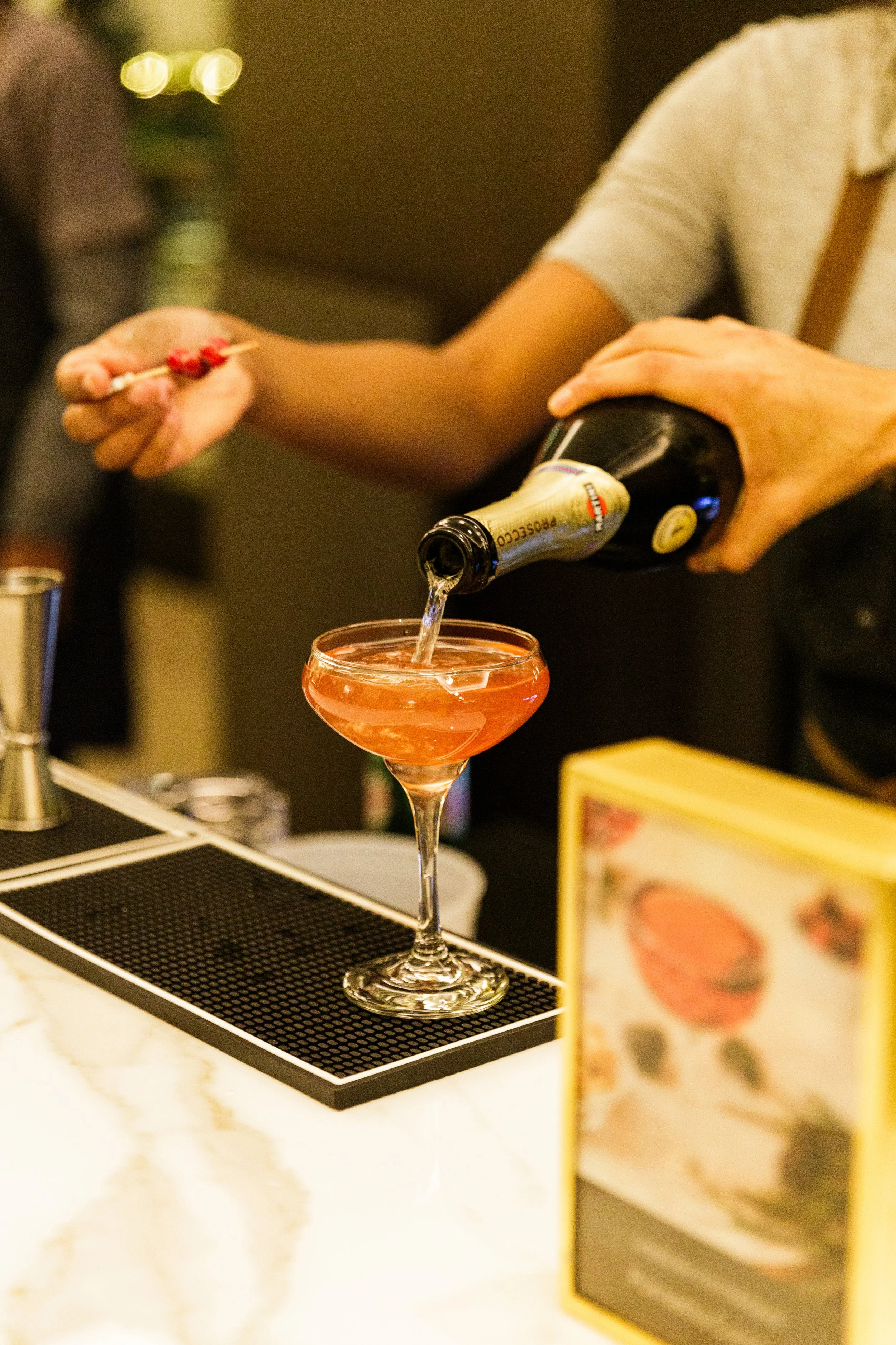 A bartender pouring a pink cocktail into a glass at a bar or event setting.