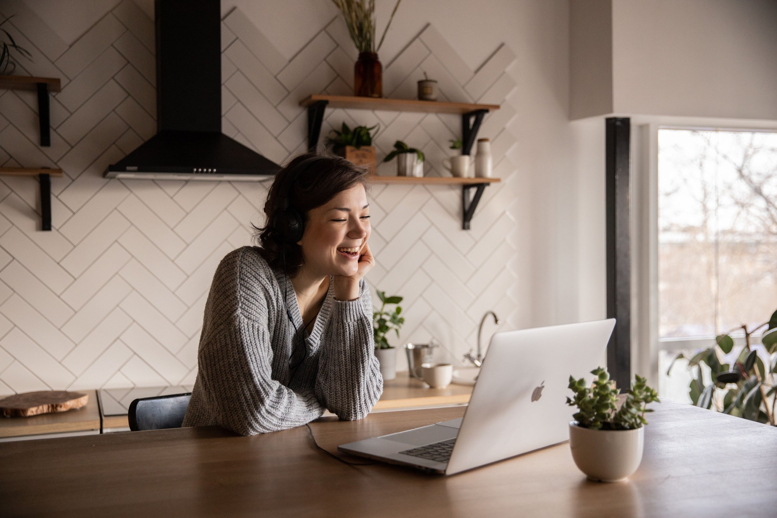 A young woman with dark hair is smiling while looking at her laptop. She is receiving an ADHD evaluation with Claricove and their clinical team.