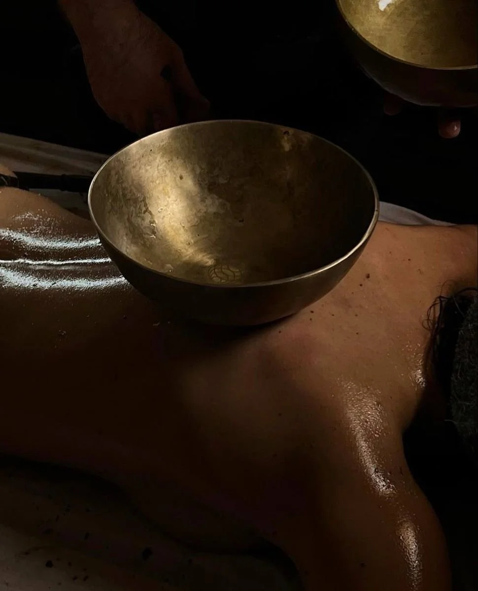 A person receiving a massage with a singing bowl placed on their back during the massage.