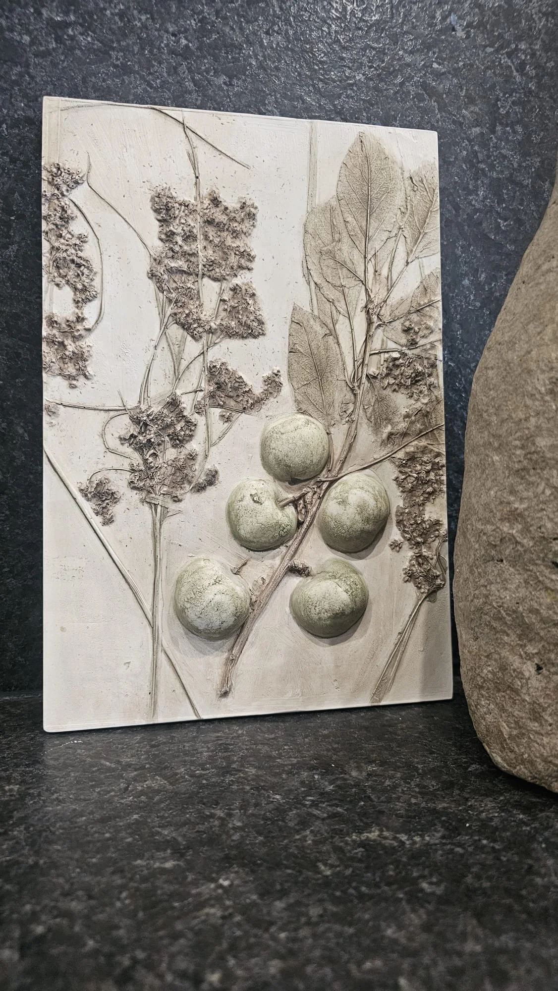 Une plaque en plâtre représentant une branche avec des feuilles et des fruits, probablement des raisins et des figues.