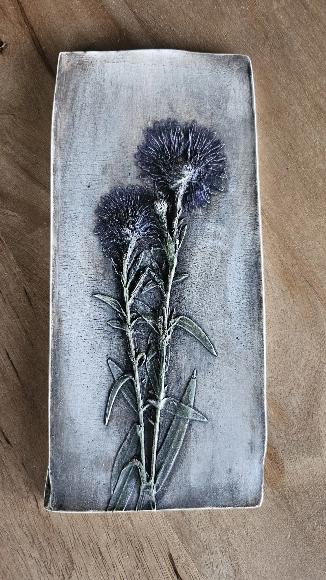 Une pièce de monnaie en forme de boîte rectangulaire avec une image de fleurs violettes dessus, posée sur une surface en bois.