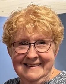 A smiling woman with glasses and short, curly red hair.