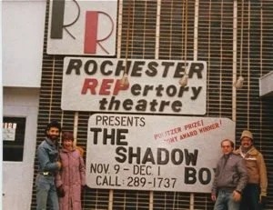 A group of four people standing outside Rochester Repertory Theatre with a large sign promoting the play "The Shadow Box" from November 9 to December 1.