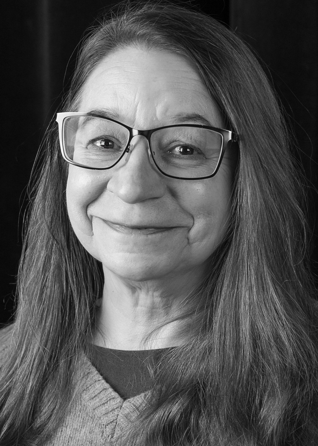 Black and white portrait of a smiling woman with long hair and glasses.