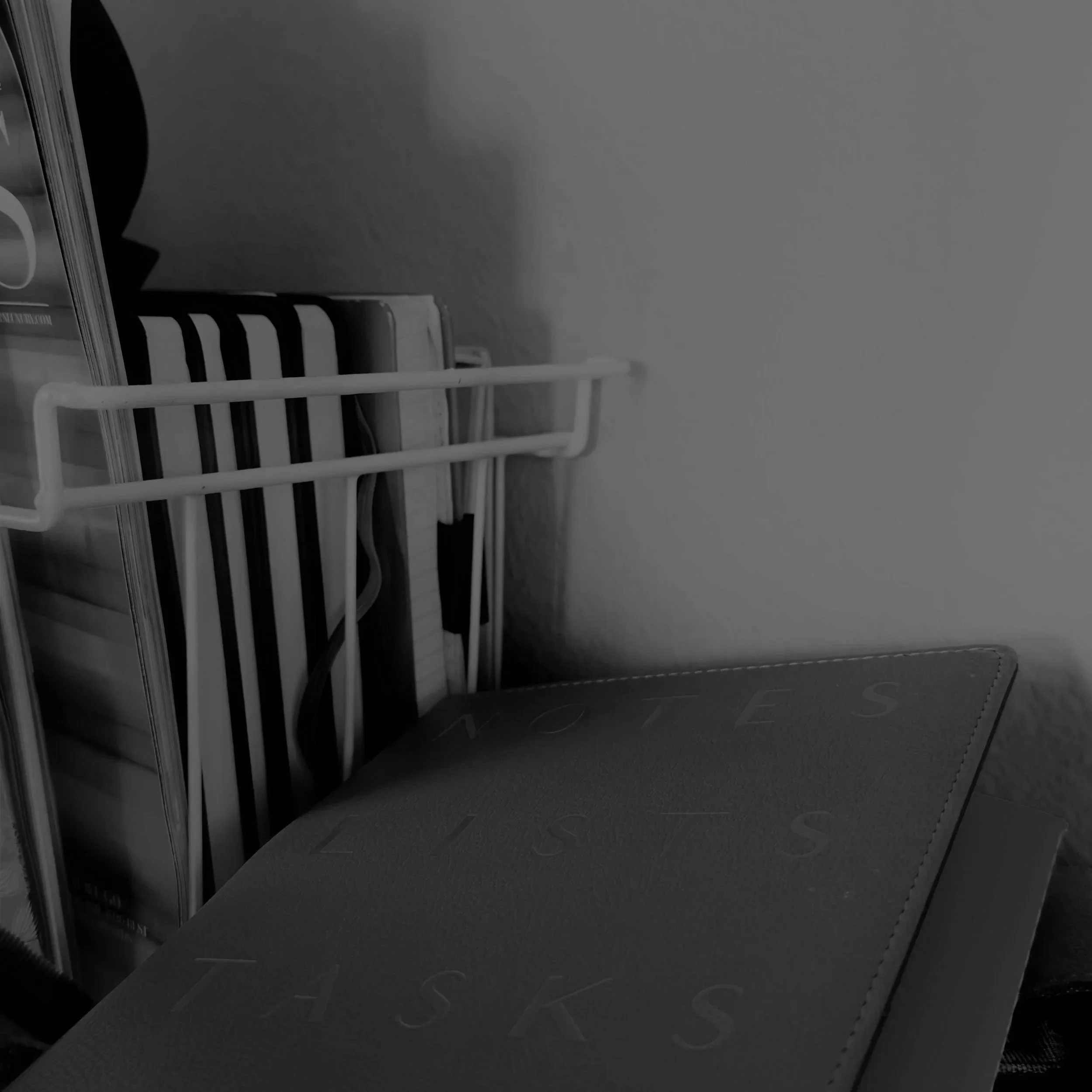 A gray room with a stack of magazines or books and a black plastic chair with vertical slats.