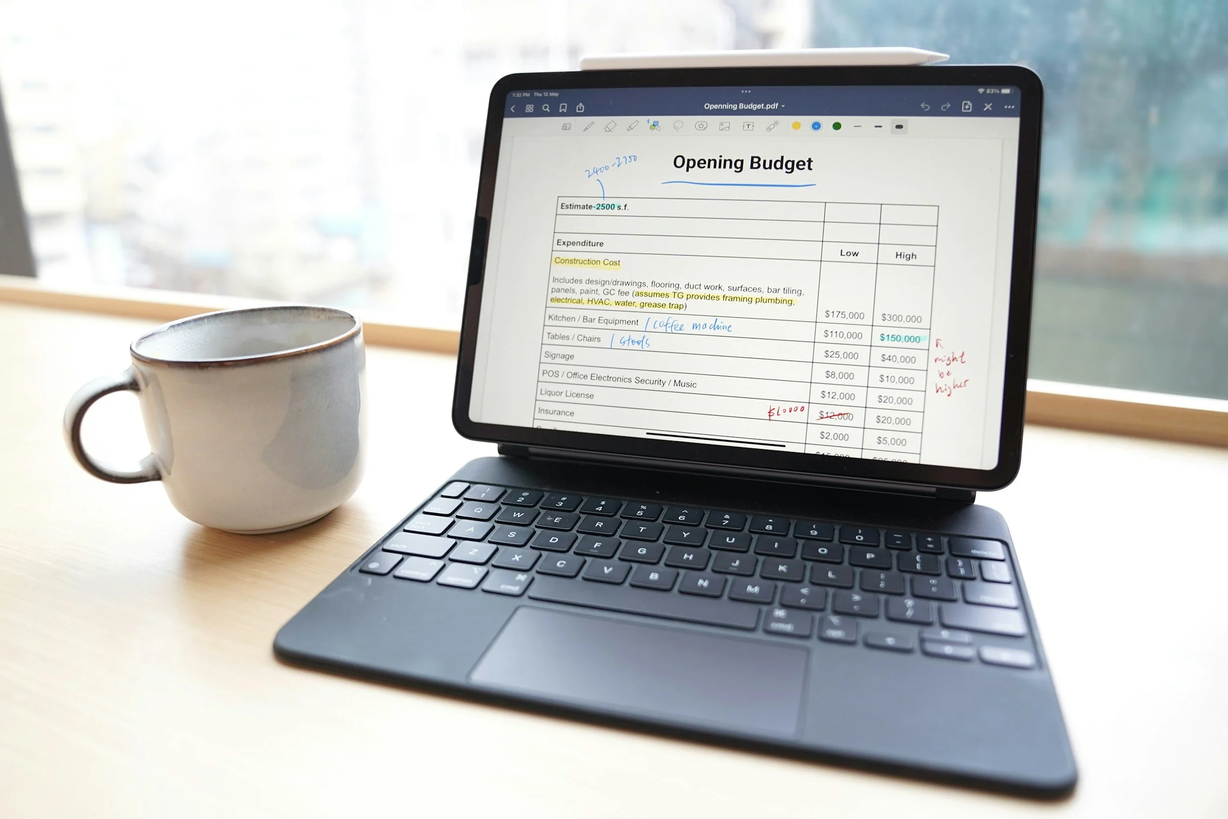 A laptop displaying a PDF document titled 'Opening Budget' with handwritten notes and highlighted text, sitting on a desk next to a white mug near a window.