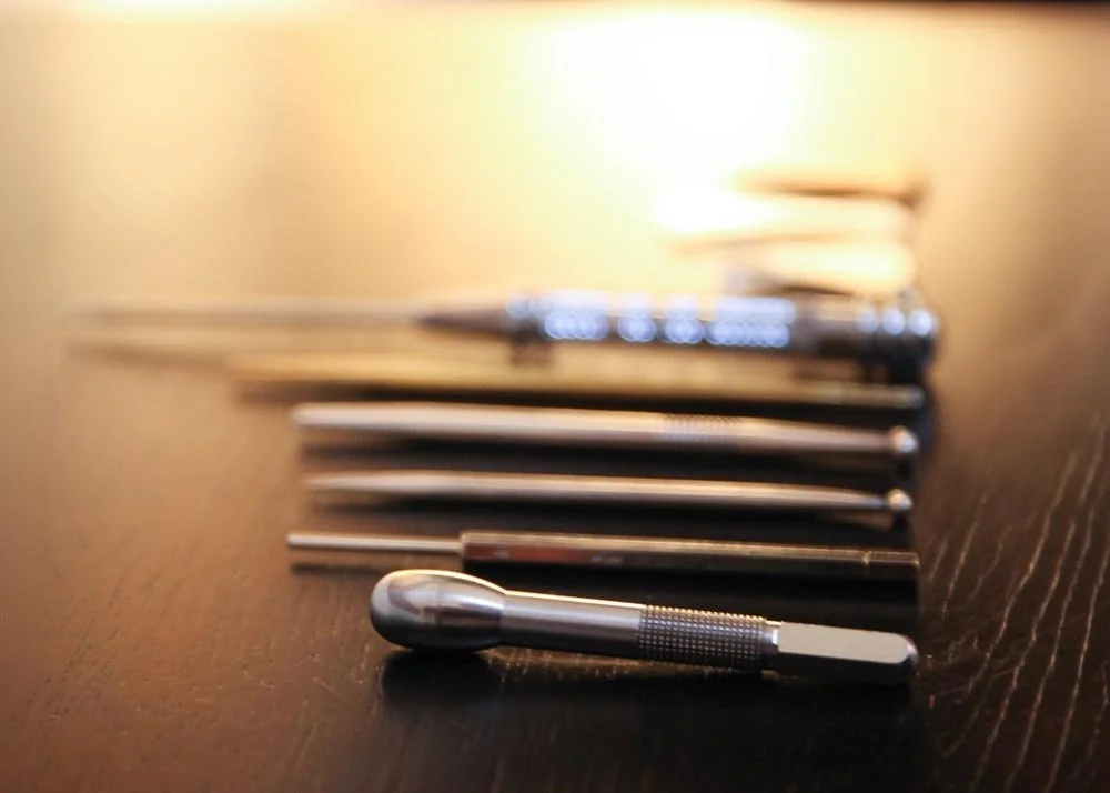 A set of metal non invasive Japanese Teishin and other metal tools and implements the size of pens or pencils arranged on a dark wooden surface.