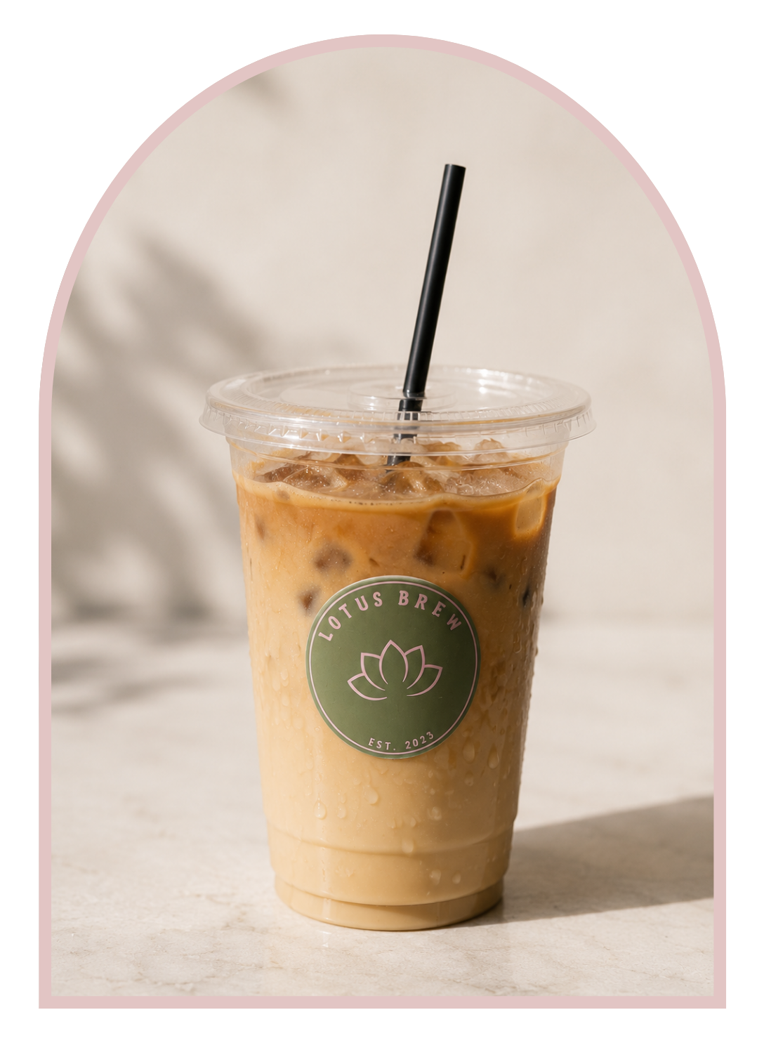 Iced coffee beverage with ice cubes in a clear plastic cup, plastic lid, and black straw, branded with Lotus Brew logo, on a light-colored surface with a neutral background.