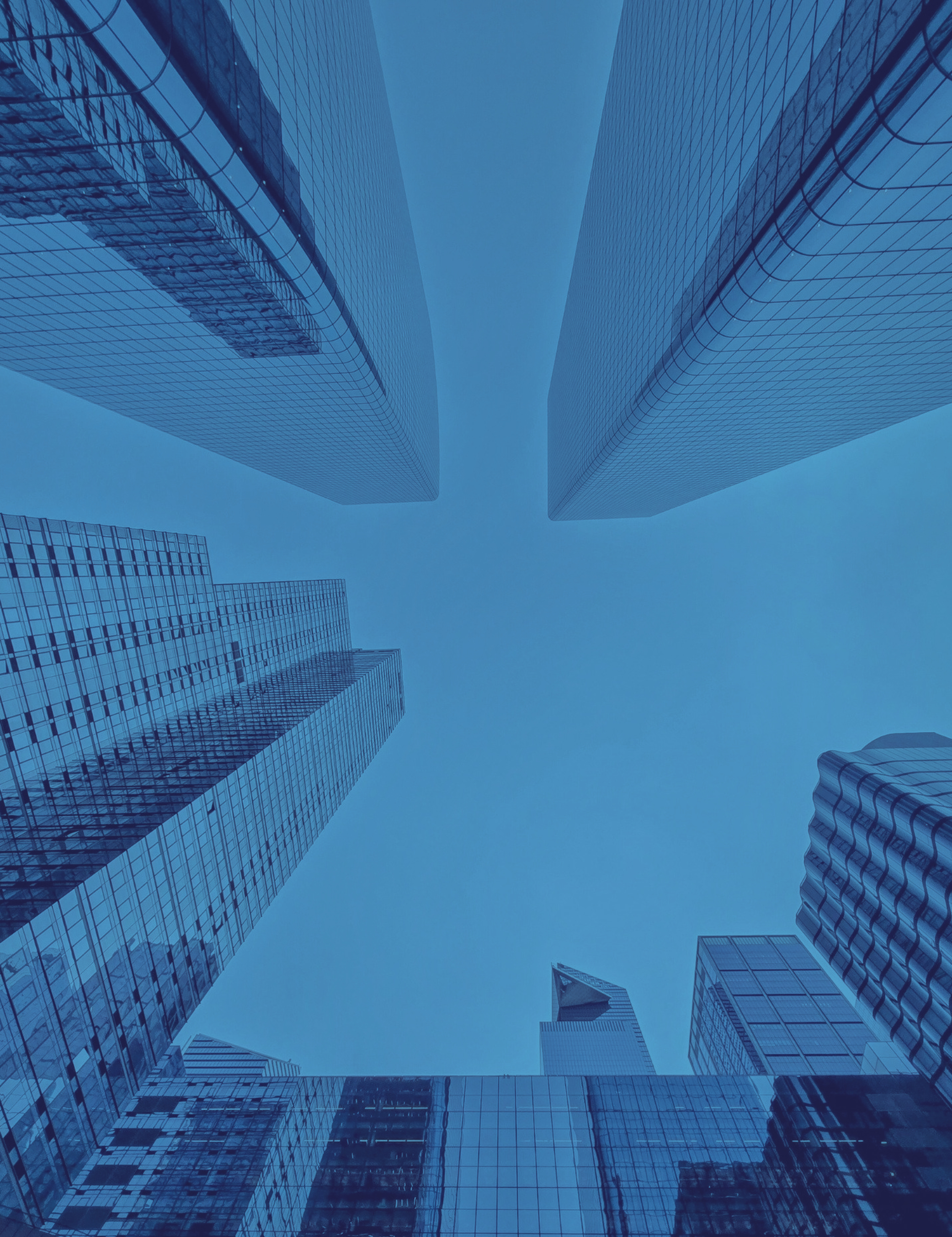 Looking up at modern glass skyscrapers in a city with blue skies.