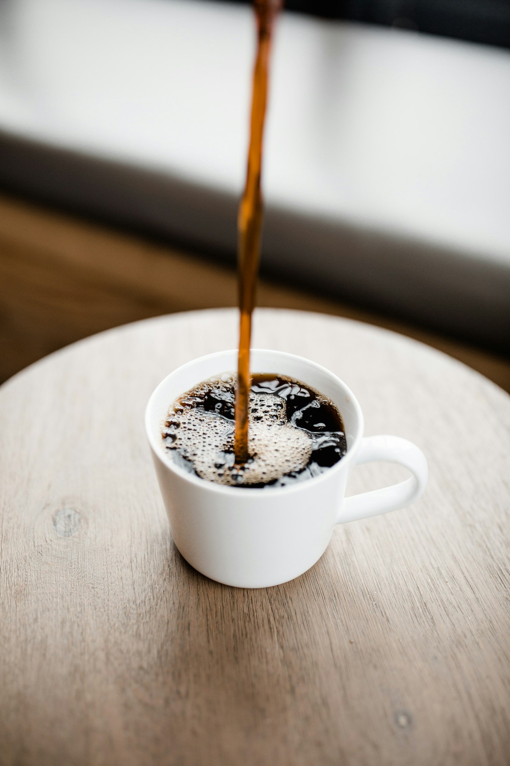 Coffee being poured into a white mug on a wooden table.