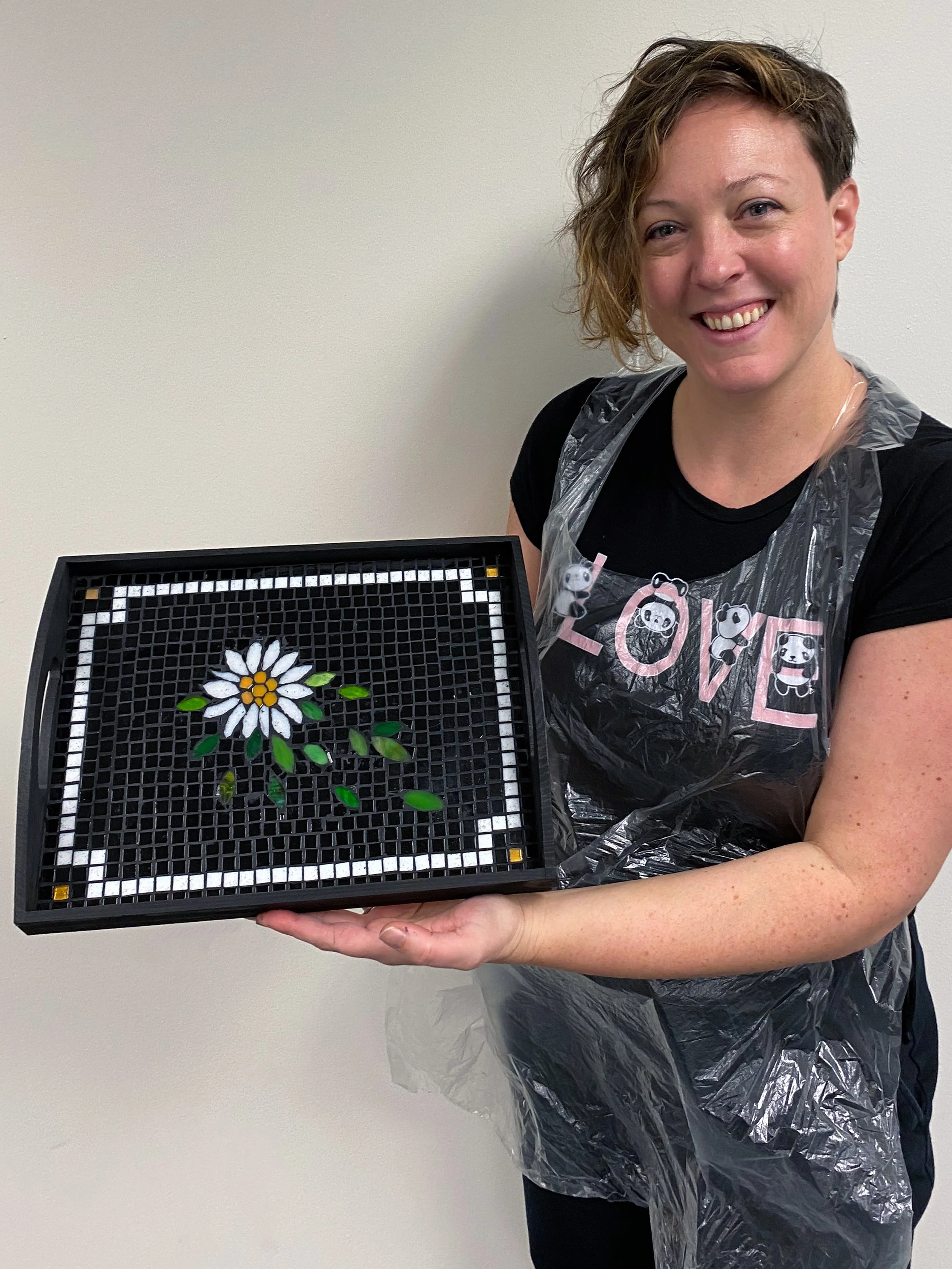 A student proudly displaying the mosaic artwork of a flower creating during a class