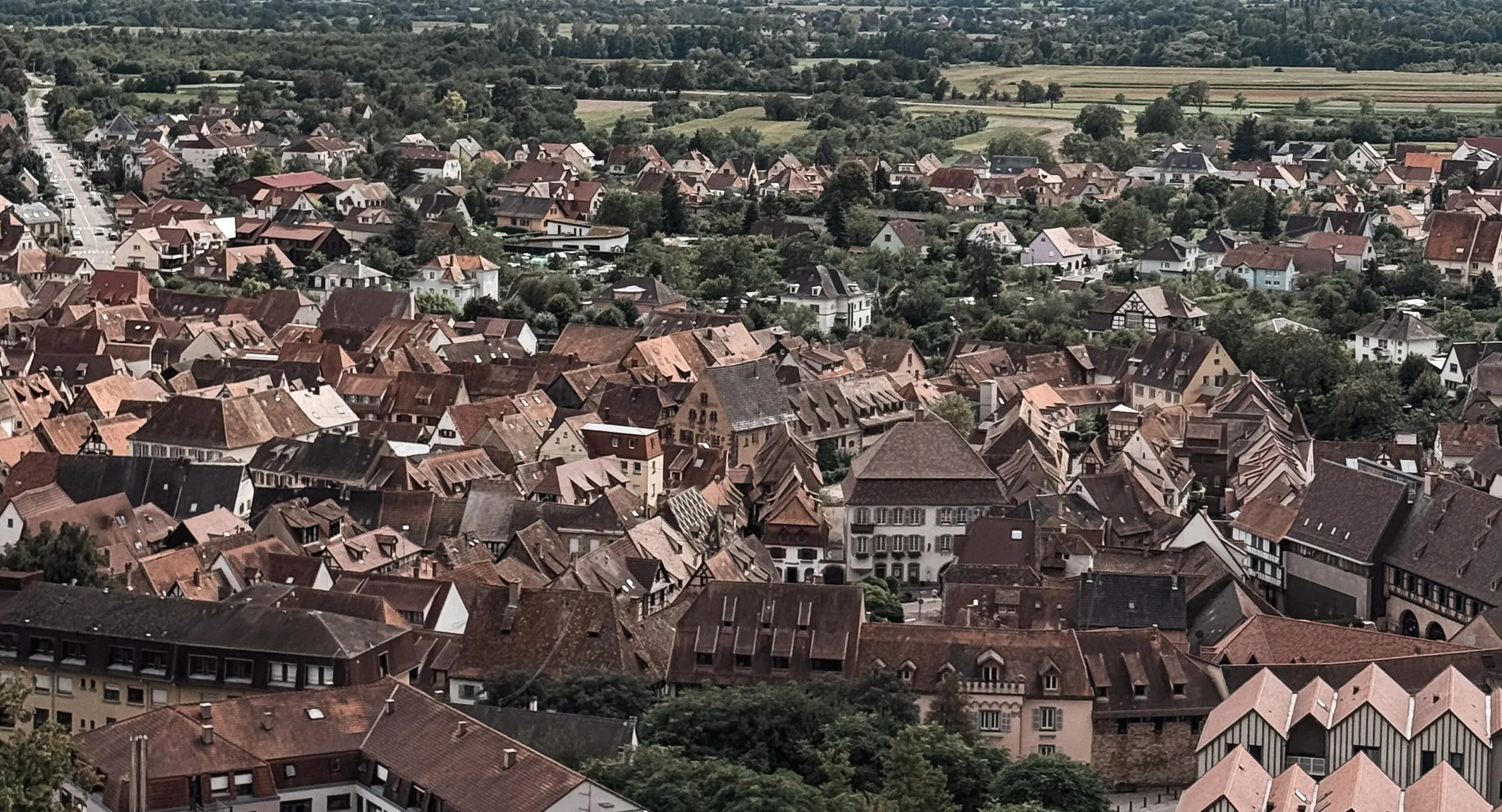 Aerial view of a European town with tightly packed buildings, many with red-tiled roofs, and surrounding green landscapes.