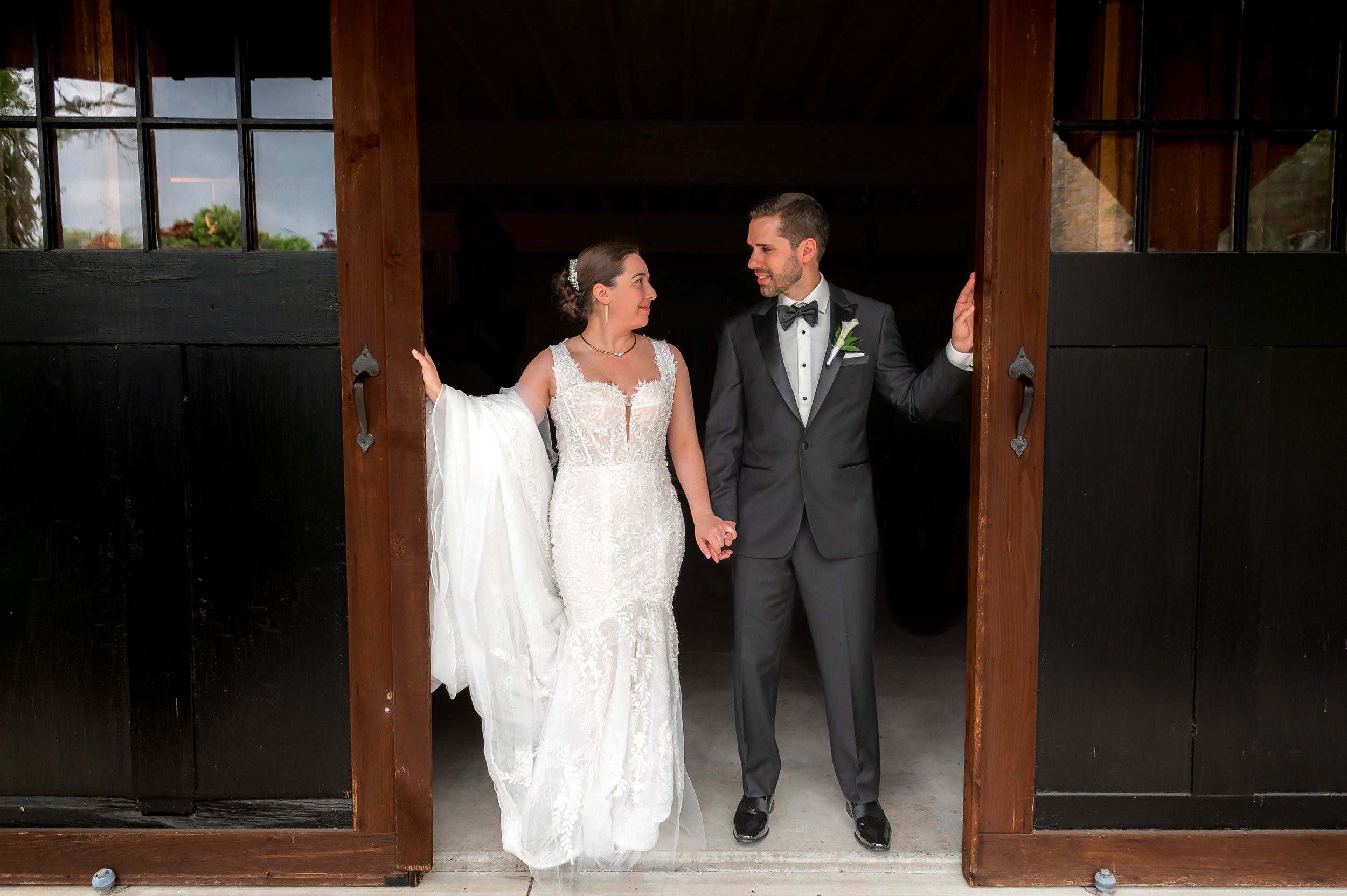 Bride and groom holding hands at a doorway at The Barn at Silverstone, Lancaster PA, outdoors in natural light.