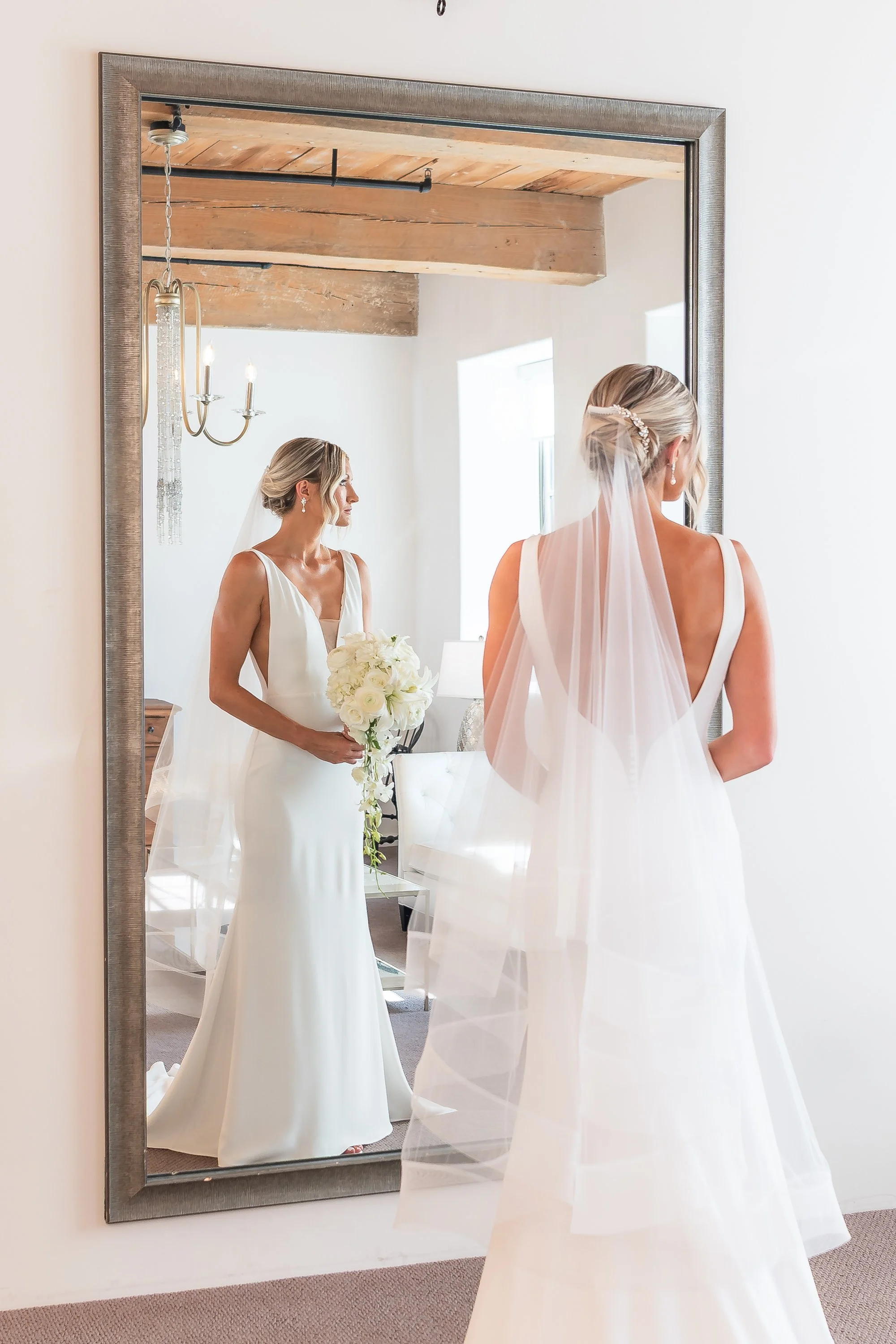 Bride admiring her reflection in a mirror at The Cork Factory, Lancaster PA, wearing a white dress and veil, holding a bouquet of white flowers.