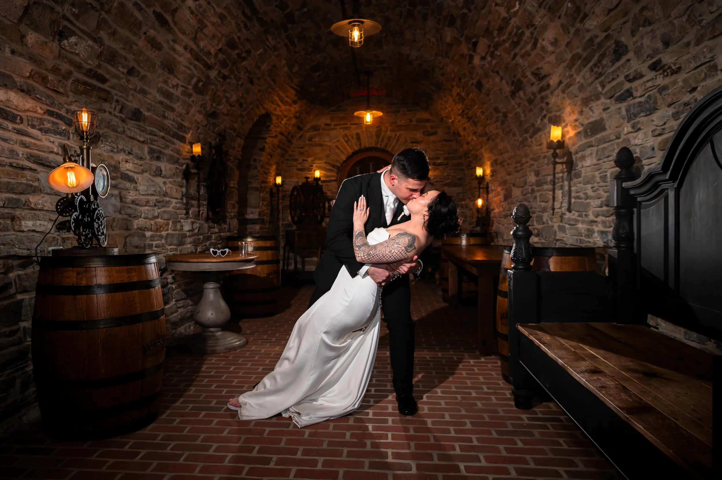 Bride and groom sharing a kiss at Stone Gables Estate's Star Barn cellar, Elizabethtown PA, rustic brick walls and warm lighting.